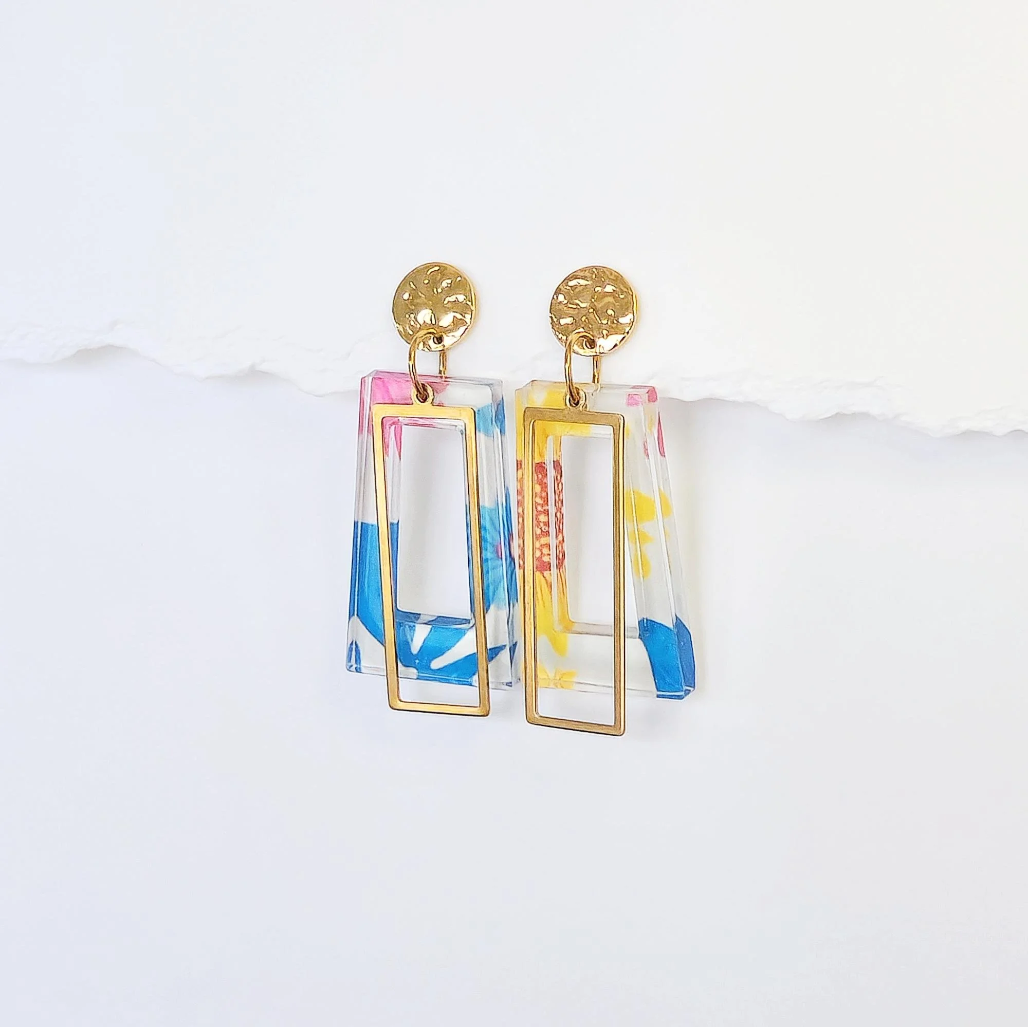 Pair of colorful, geometric dangle earrings with gold accents, featuring rectangular shapes and abstract patterns in blue, yellow, pink, and red.