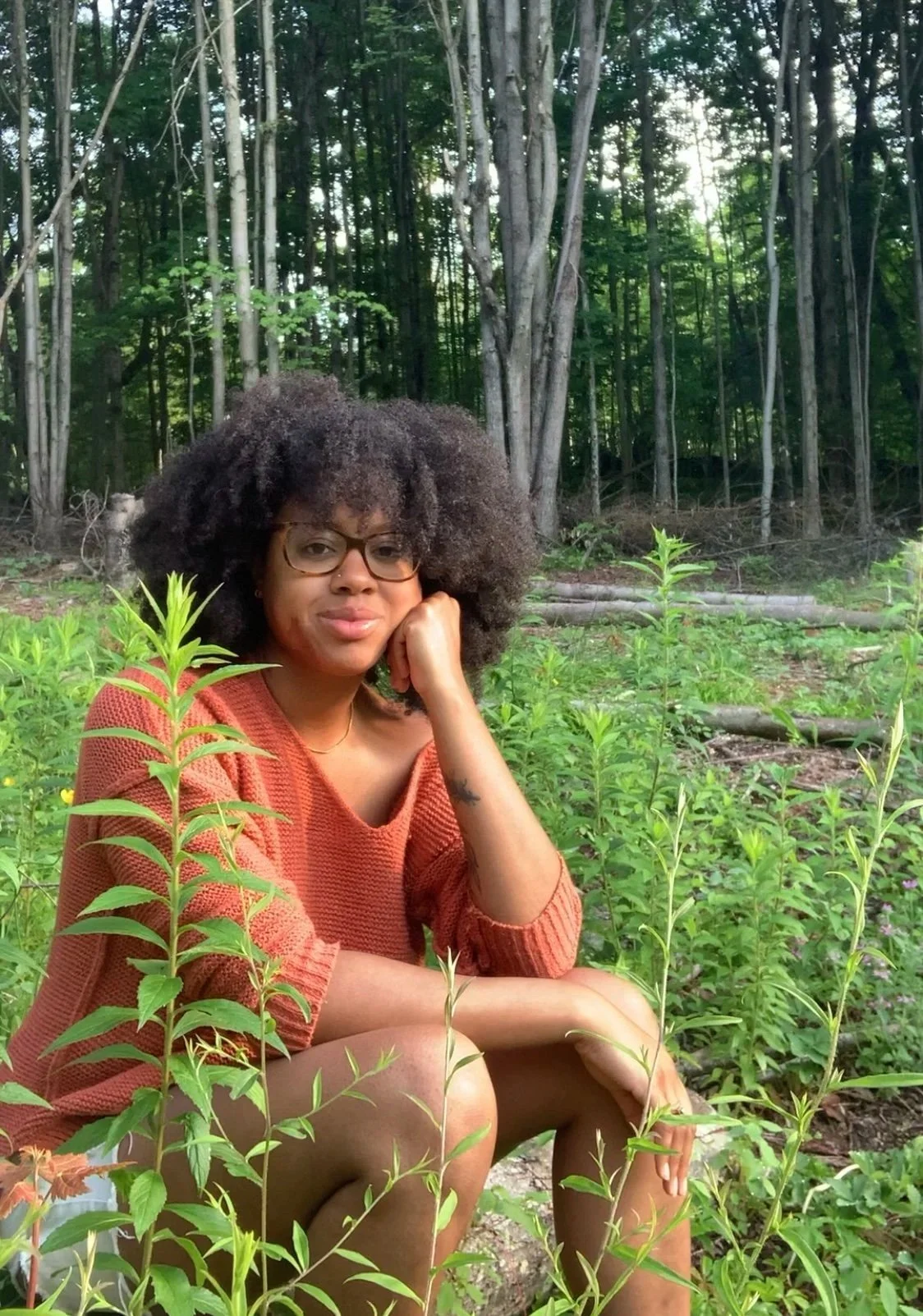 A Black woman sits with plants on her off grid homestead