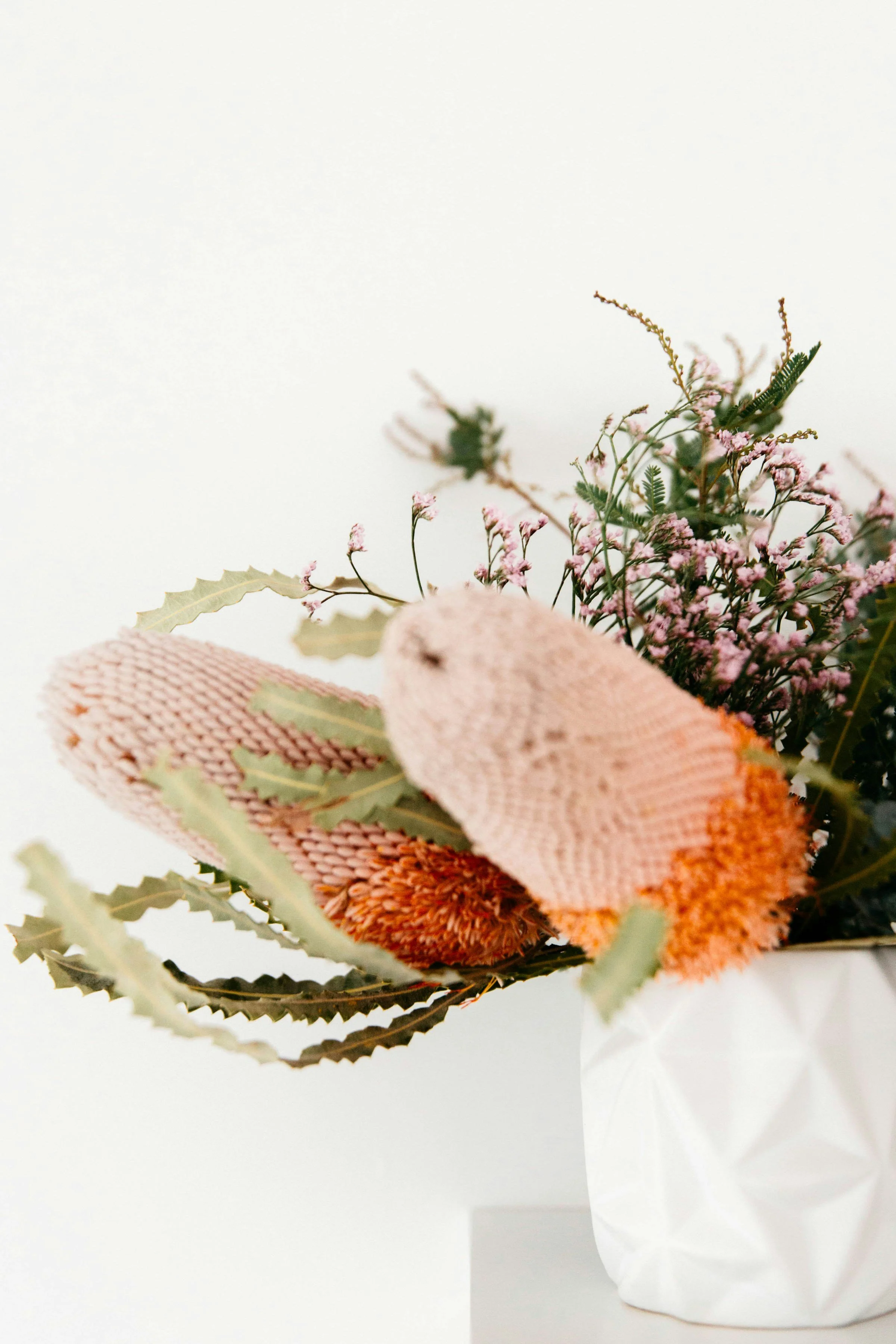 A bouquet of pink and green flowers in a pink burlap wrapped container placed on white surface