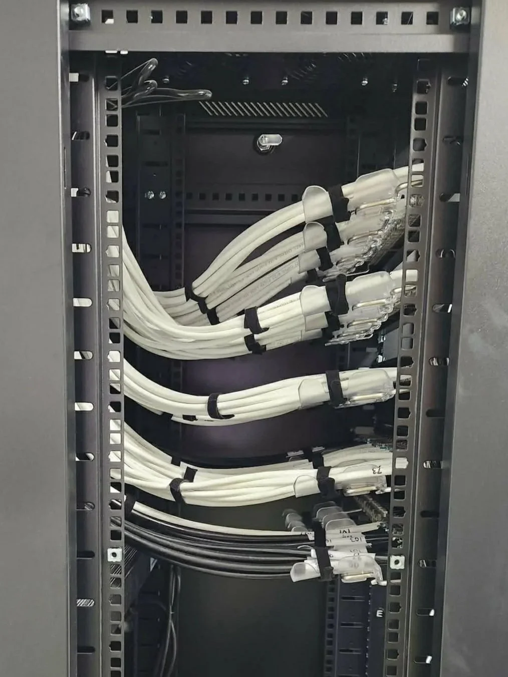 Inside of a network rack with white and black cables organized and secured with cable ties.