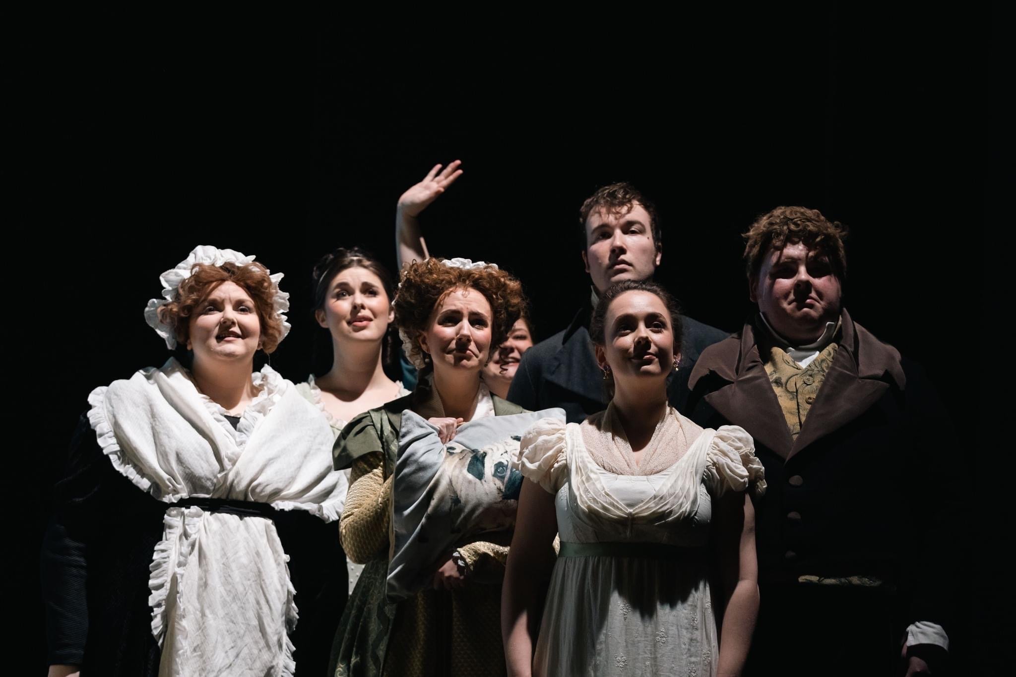 Actors dressed in period costumes on stage during a theater performance, under dramatic lighting.