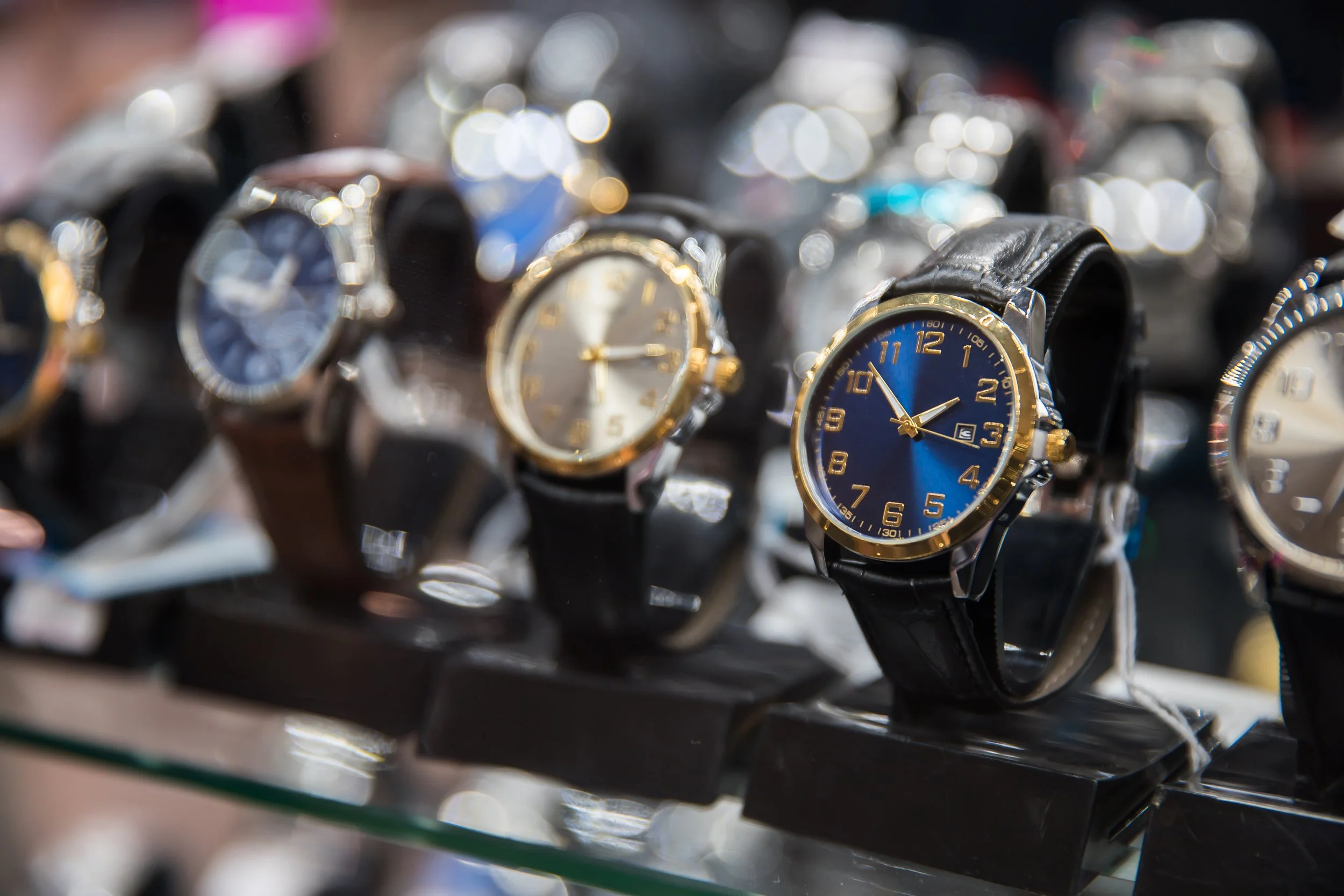 Display of multiple wristwatches on a store shelf, with one blue-faced watch prominently in the foreground.