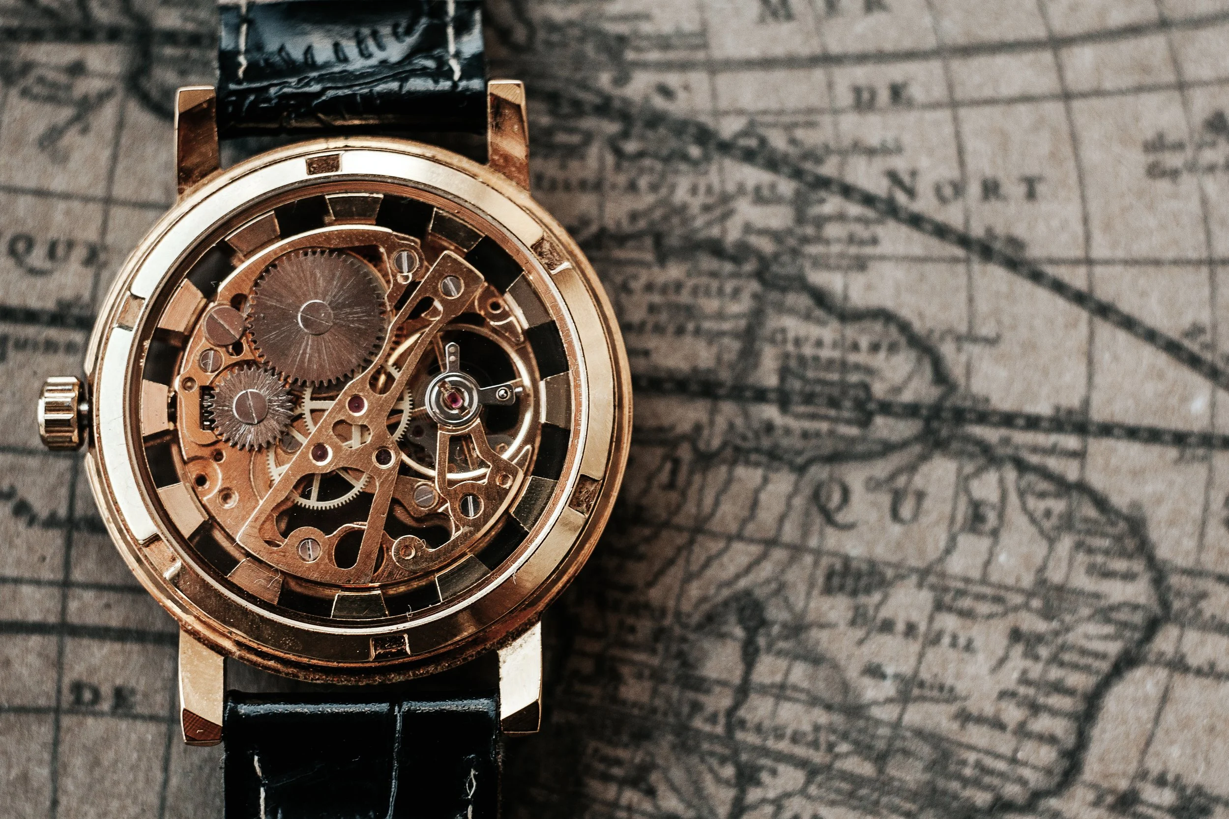 A close-up of a gold mechanical wristwatch with a skeleton dial, showing the internal gears and mechanisms, on a vintage map background.