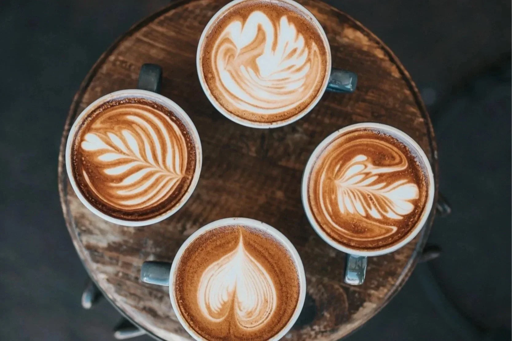 Four cups of coffee with latte art, placed on a round wooden table.