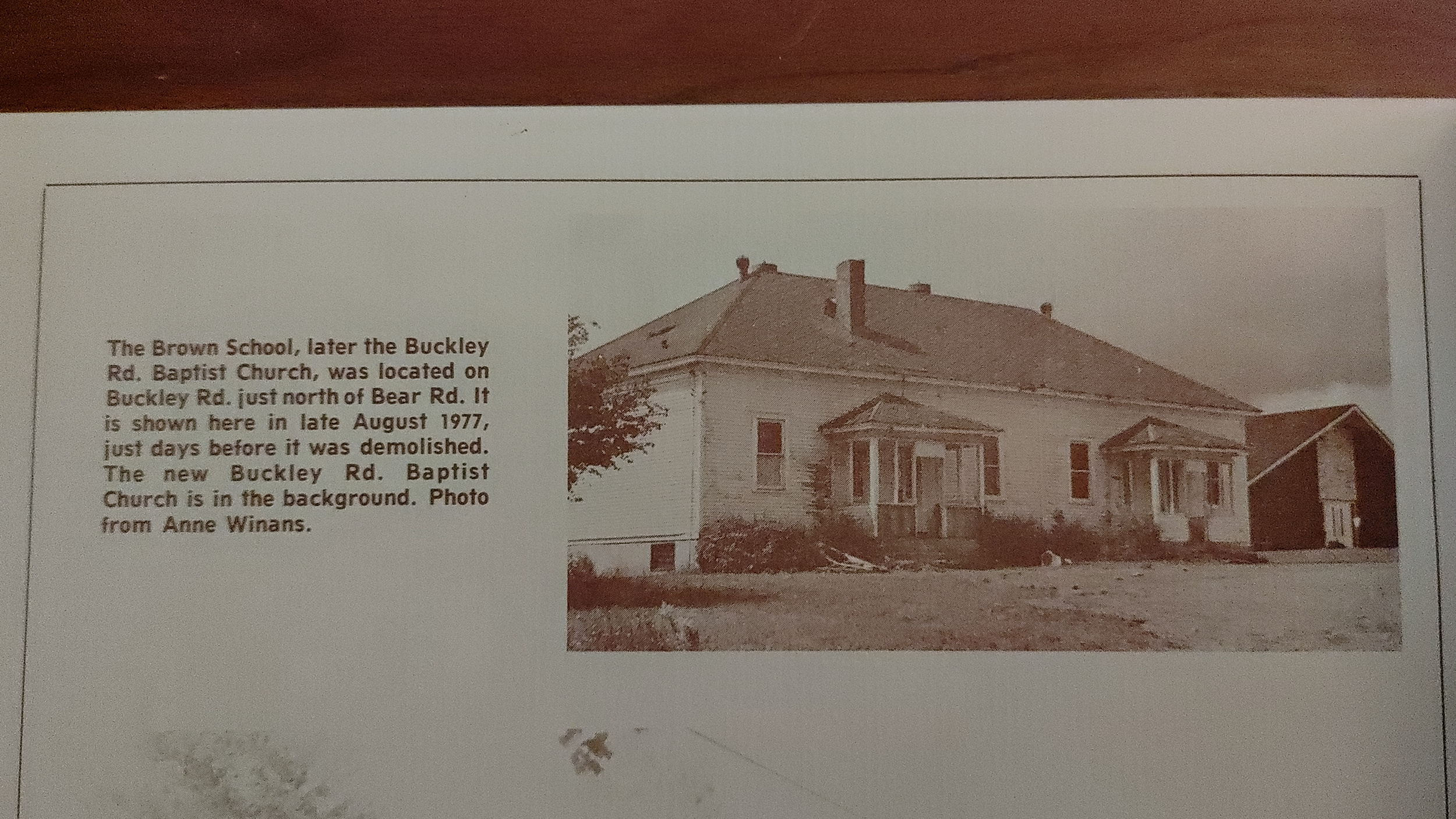 An old black and white photograph of the Brown School, later the Buckley Rd. Baptist Church, depicting a large, two-story house with a porch and multiple windows, with trees and a shed nearby. The photograph is dated August 1977 and is accompanied by