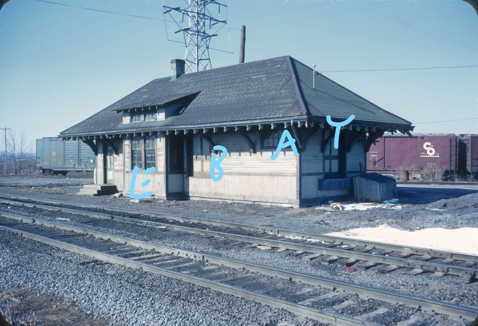 An old train station building beside train tracks with handwritten annotations marking the letters E, B, A, and T on the structure.