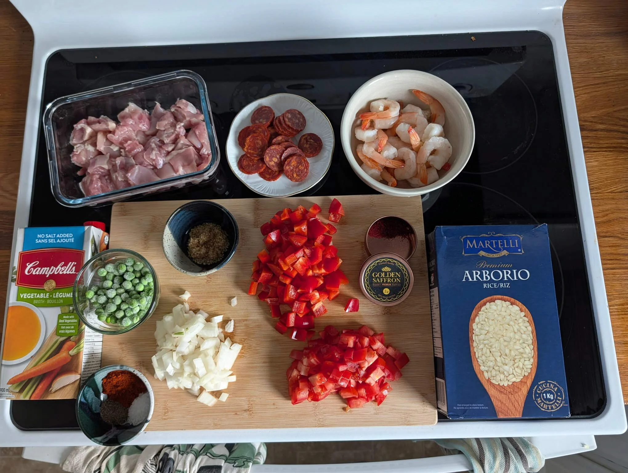 Raw paella ingredients including chorizo, shrimp, diced red pepper, onion, saffron, and Arborio rice arranged on a cutting board
