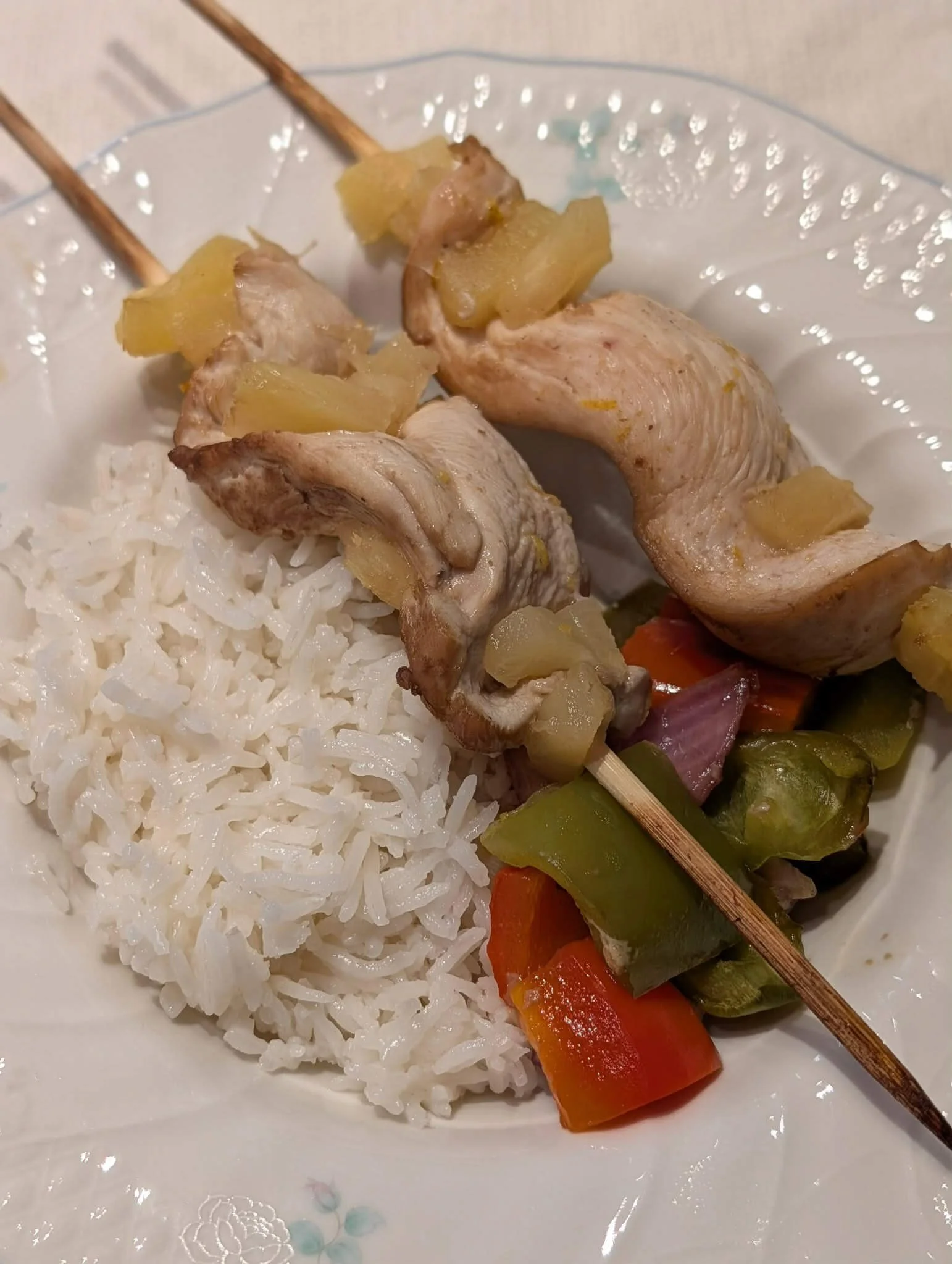 Rum-marinated chicken and pineapple skewers hung on a wire rack over peppers and onions before baking