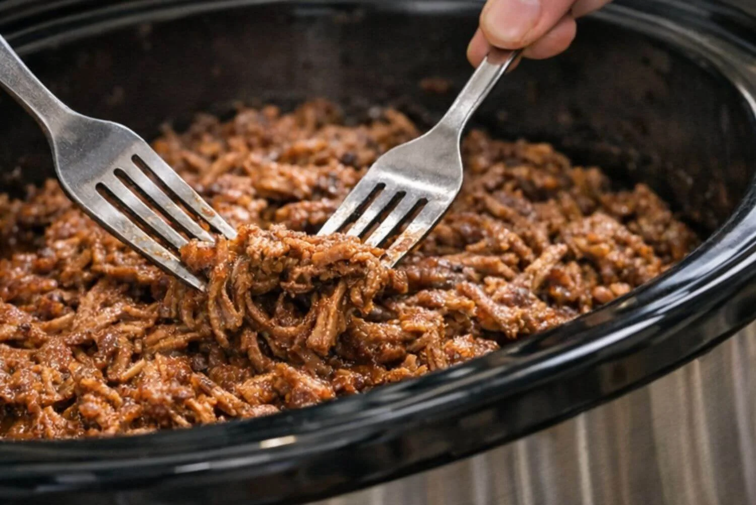 Two forks pulling tender smoky pulled pork in a slow cooker