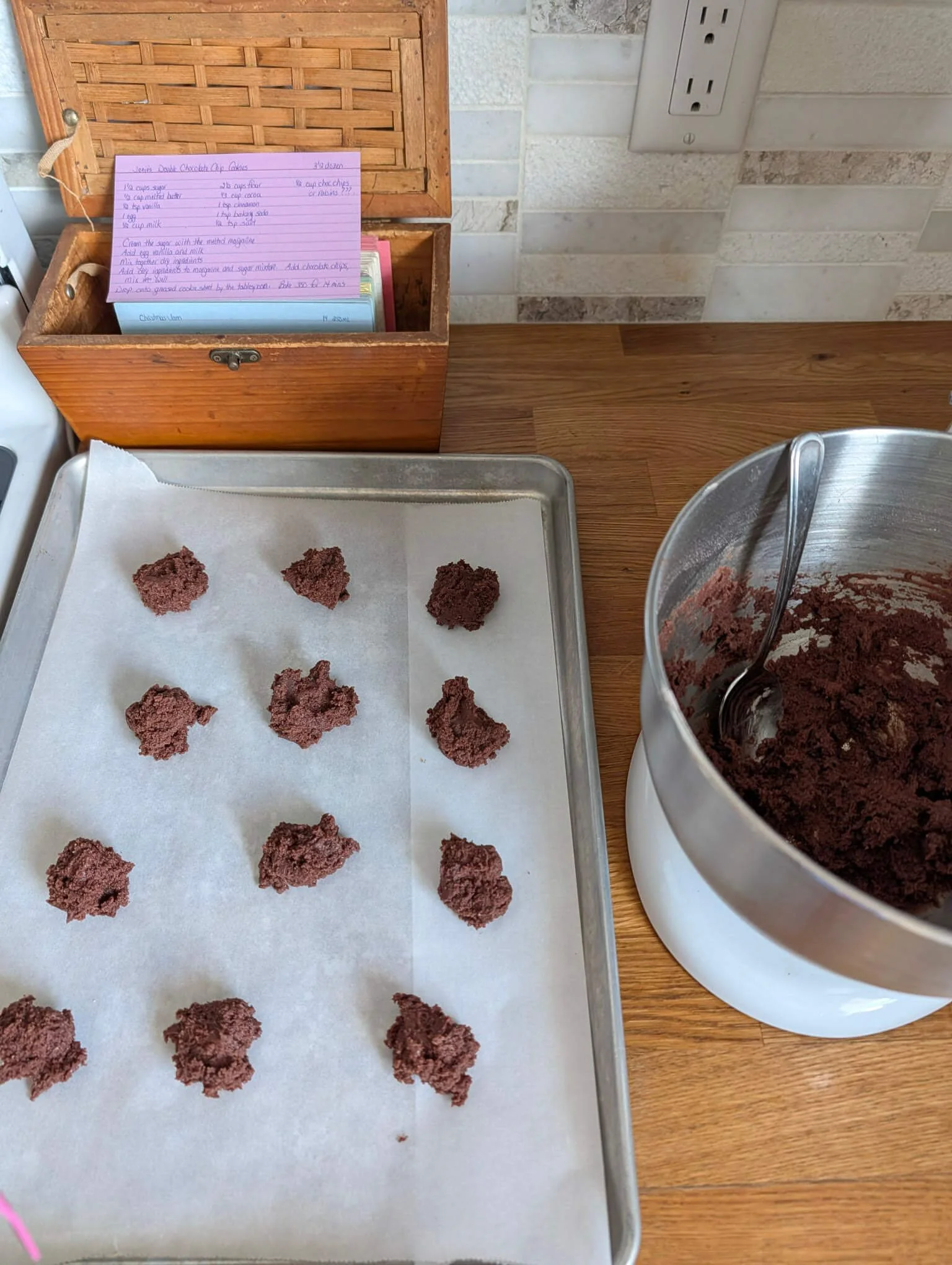 Chocolate cookie dough portioned onto a parchment-lined baking sheet next to the mixing bowl