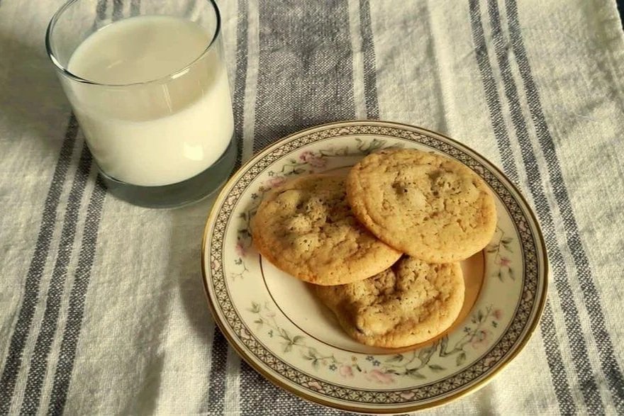 Homemade chocolate chip cookies on a floral china plate with a glass of cold milk on a striped linen cloth