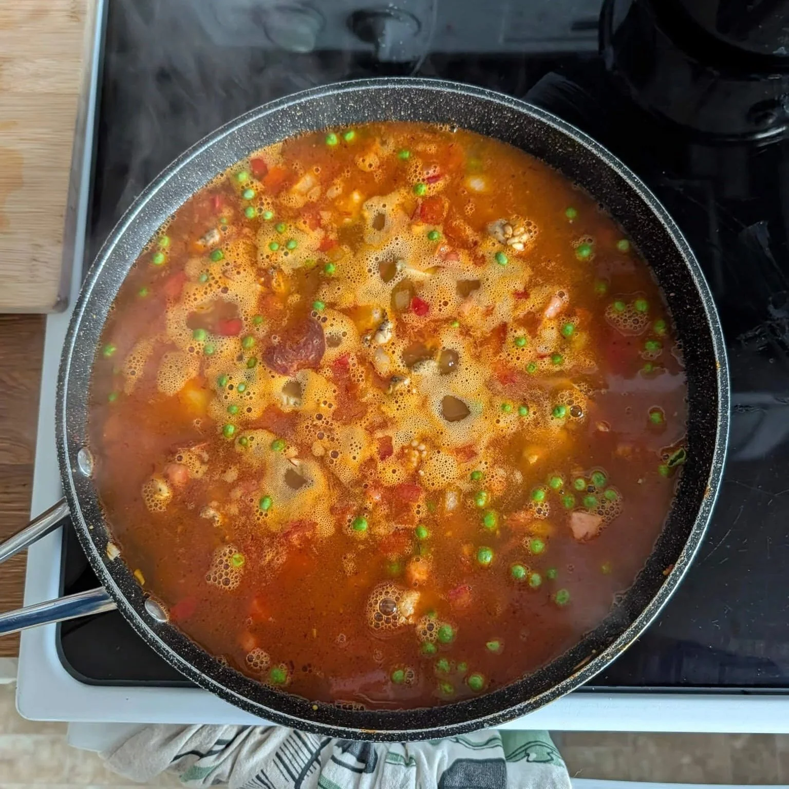 Paella simmering in a skillet with tomato broth, peas, and chorizo before the rice fully absorbs the liquid