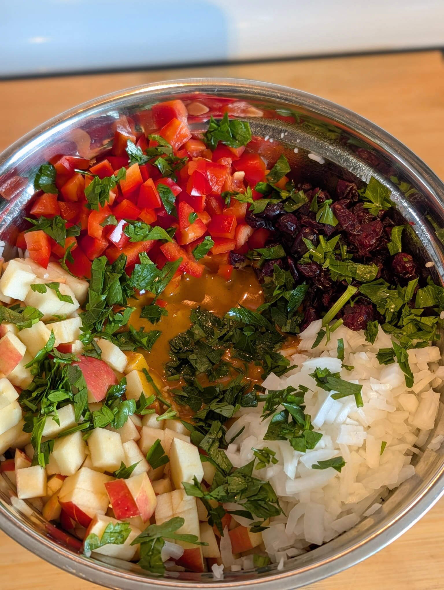 Chopped apple, red pepper, dried cranberries, onion, and parsley in a mixing bowl for curried rice salad