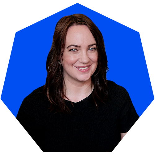 A woman with shoulder-length brown hair, wearing a black shirt, smiling in front of a blue background with a geometric shape.