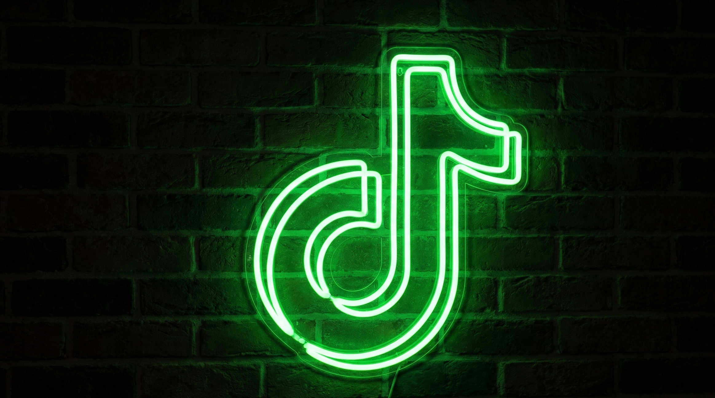 A realistic green neon light fixture in the shape of the TikTok icon, illuminating a dark brick background with a vibrant green glow.