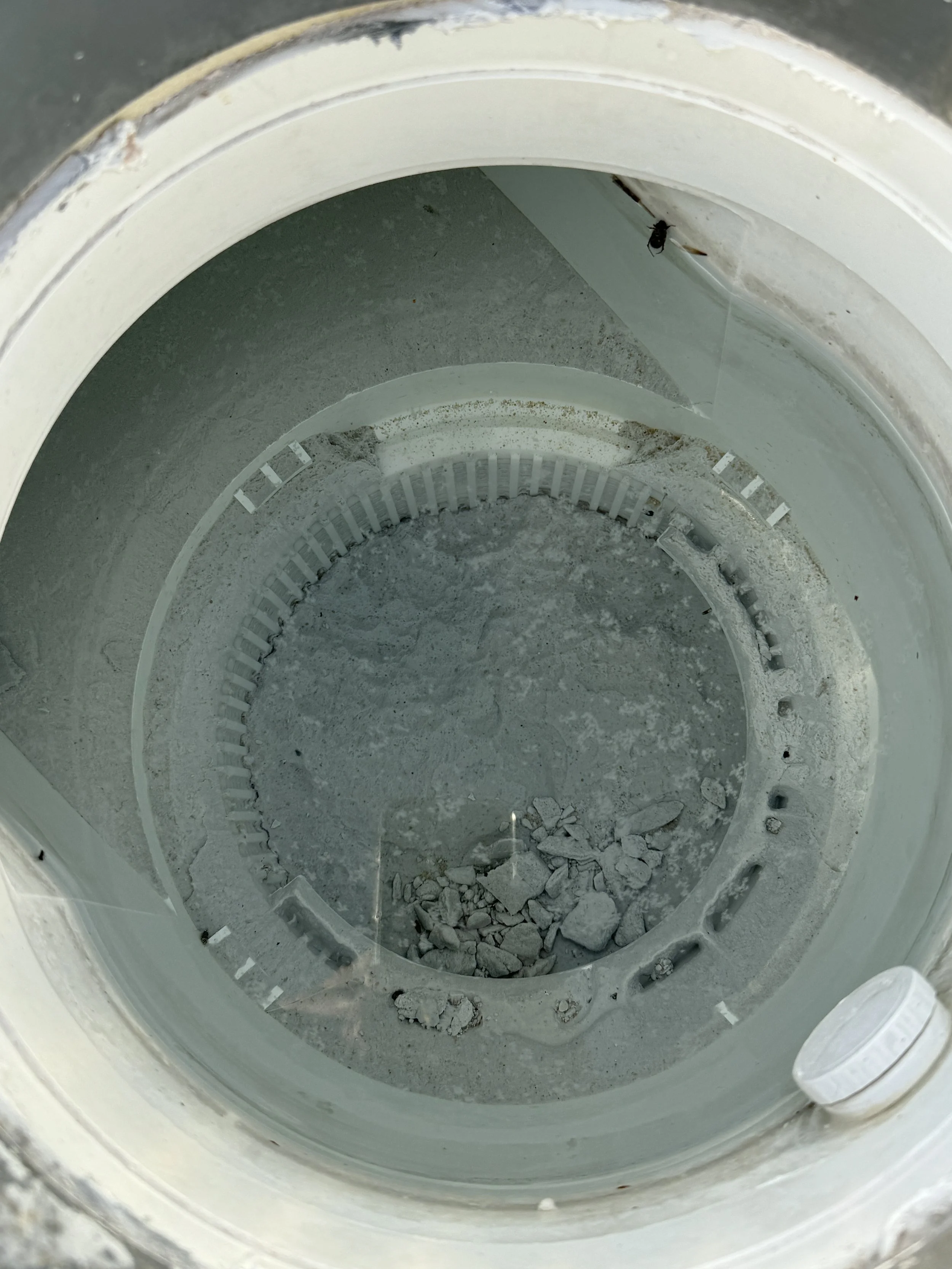 Inside of a washing machine drum, with some debris and dirt at the bottom.