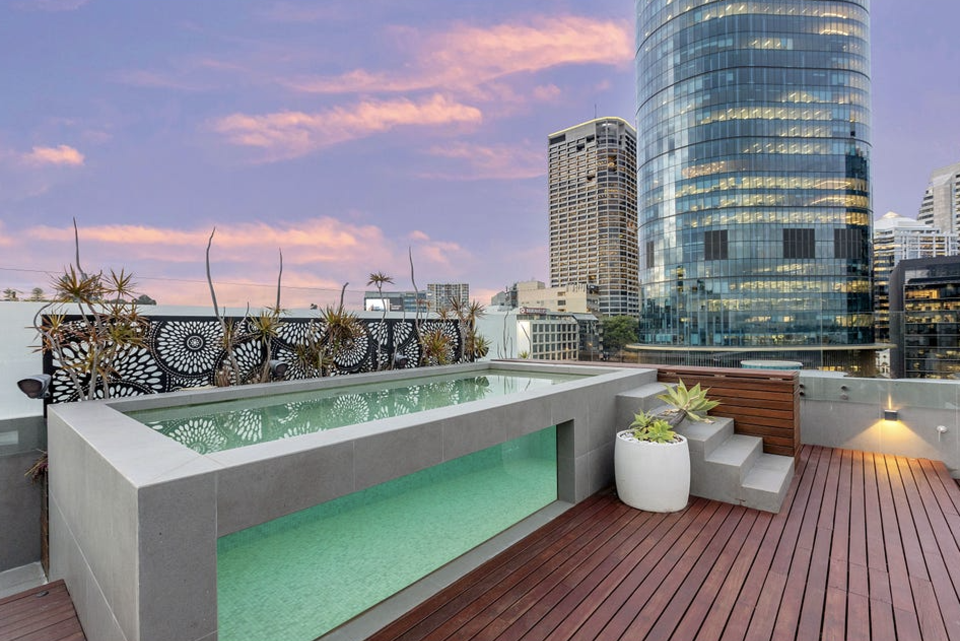 Rooftop pool with city skyline and tall glass skyscrapers during pink sunset