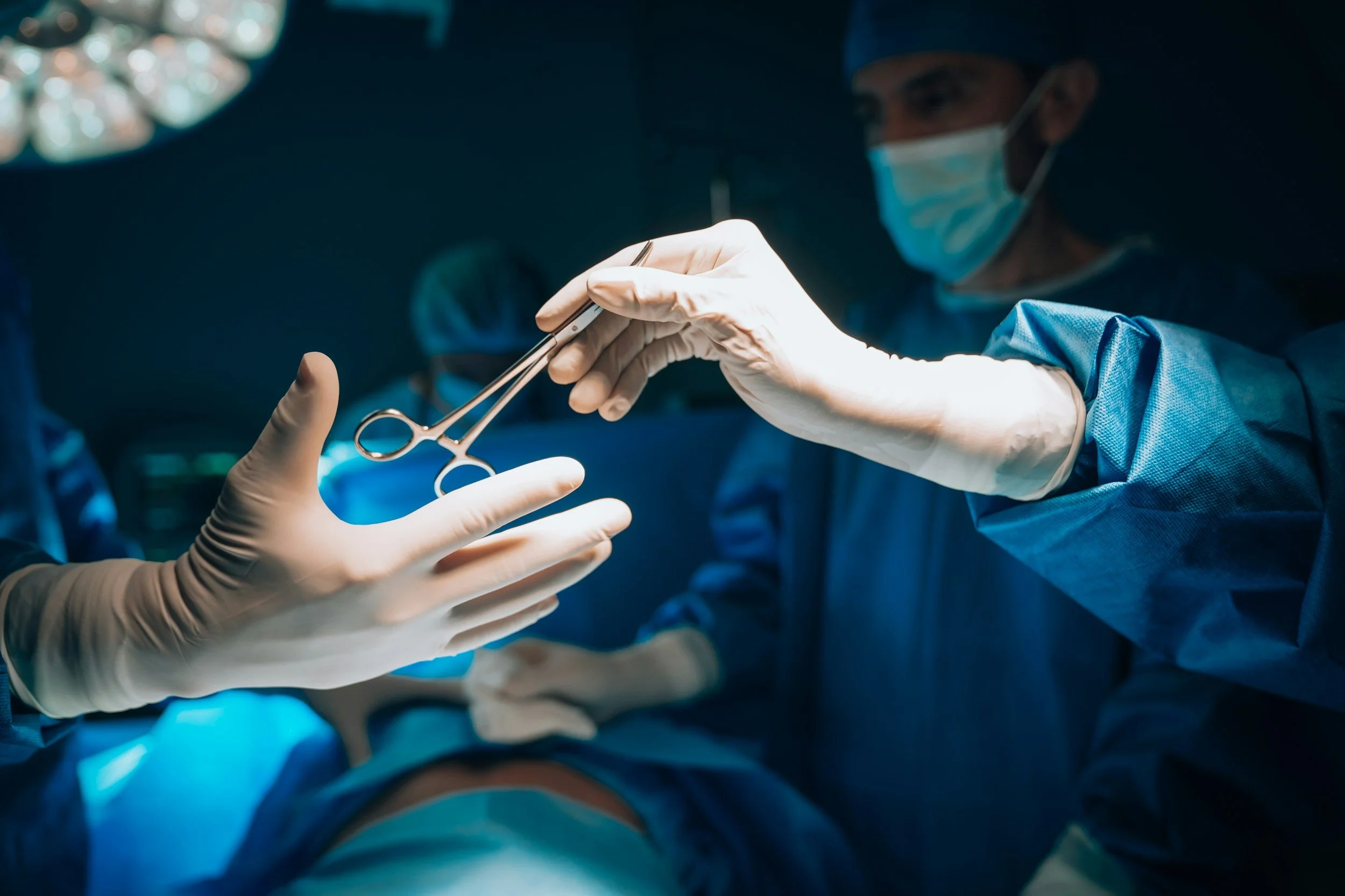 Surgeons performing an operation in an operating room, wearing surgical masks and gloves.