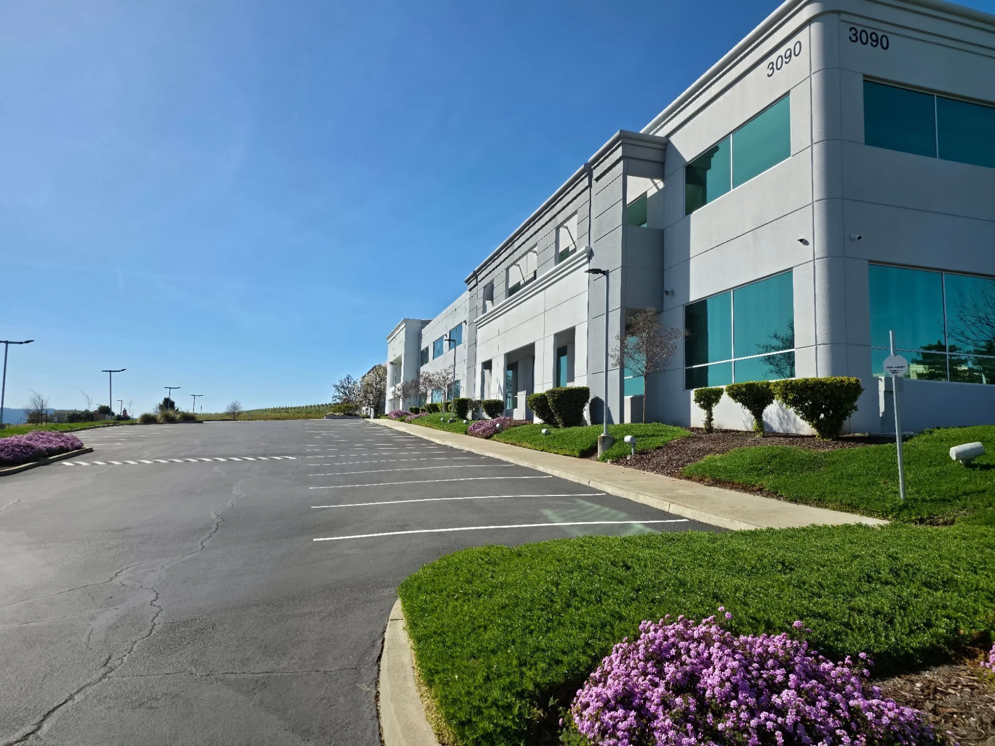 Empty parking lot in front of a modern white office building under a clear blue sky.