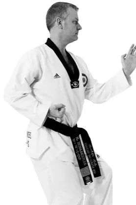 Martial artist wearing a white gi and black belt, showing a ready stance with one hand extended and the other at the waist.