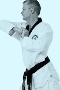A male martial artist in a white gi with a black belt, performing a martial arts move.