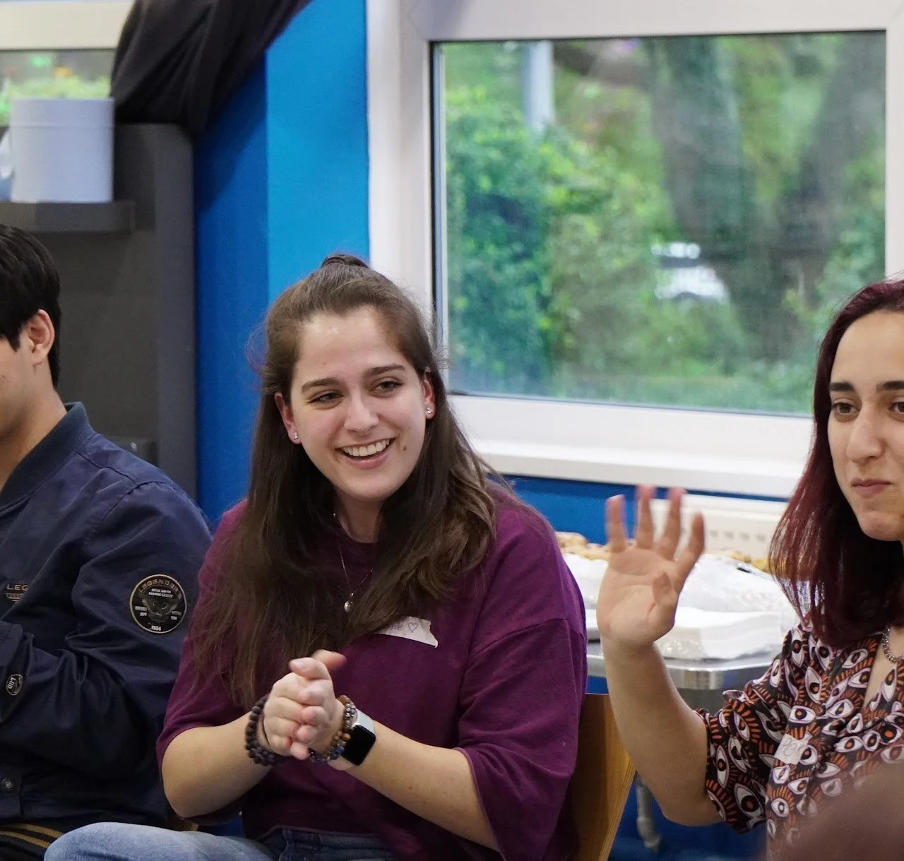 Event facilitator engaging participants during an indoor entertainment workshop, smiling and clapping along with a small group activity.