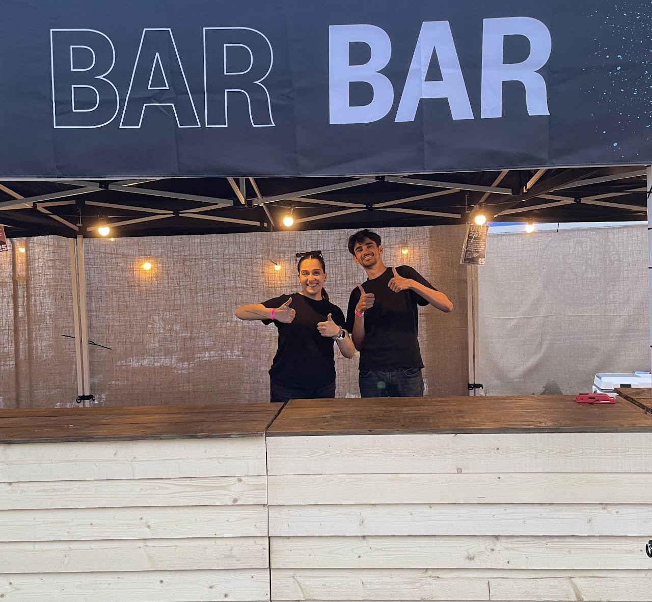 Bar team ready for service at an outdoor event, standing behind a pop-up bar during setup.