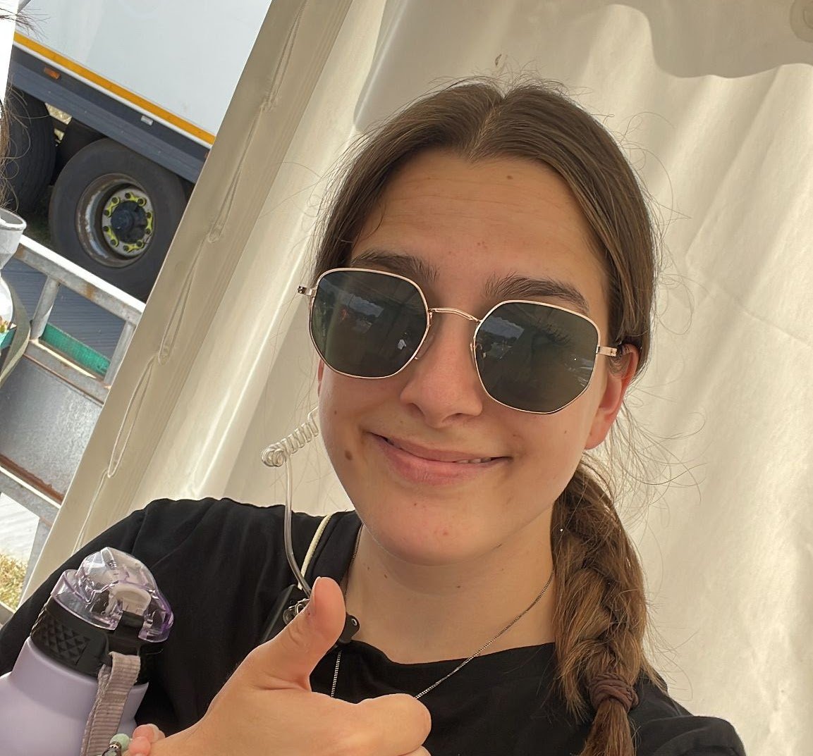 Event staff member on site giving a thumbs up during a live outdoor event, wearing radio and crew gear.