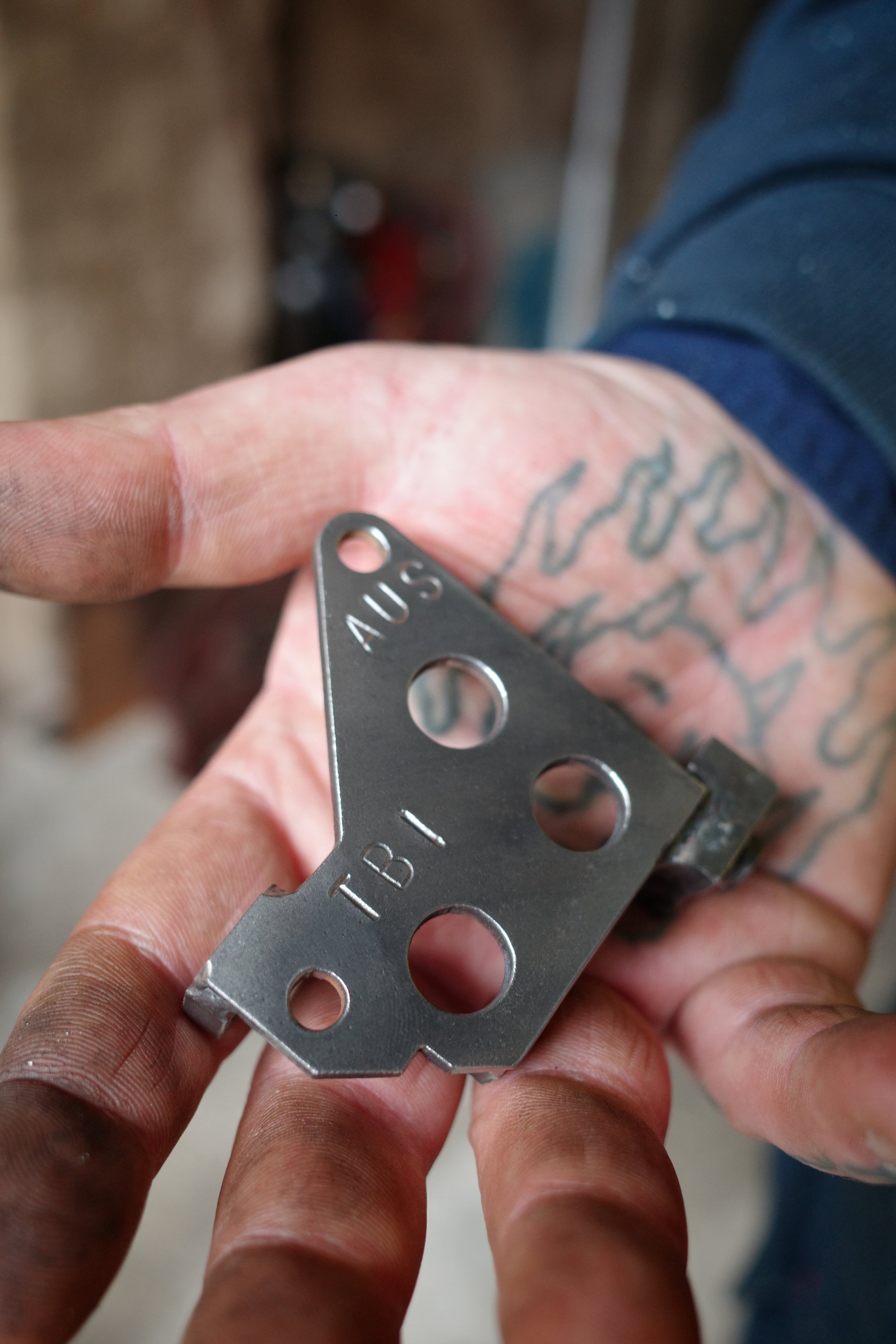 Close-up of a person's hand holding a small metallic object, which appears to be a part of a tool or a device, with the word 'AUS' and part of the word 'TIB' engraved on it.