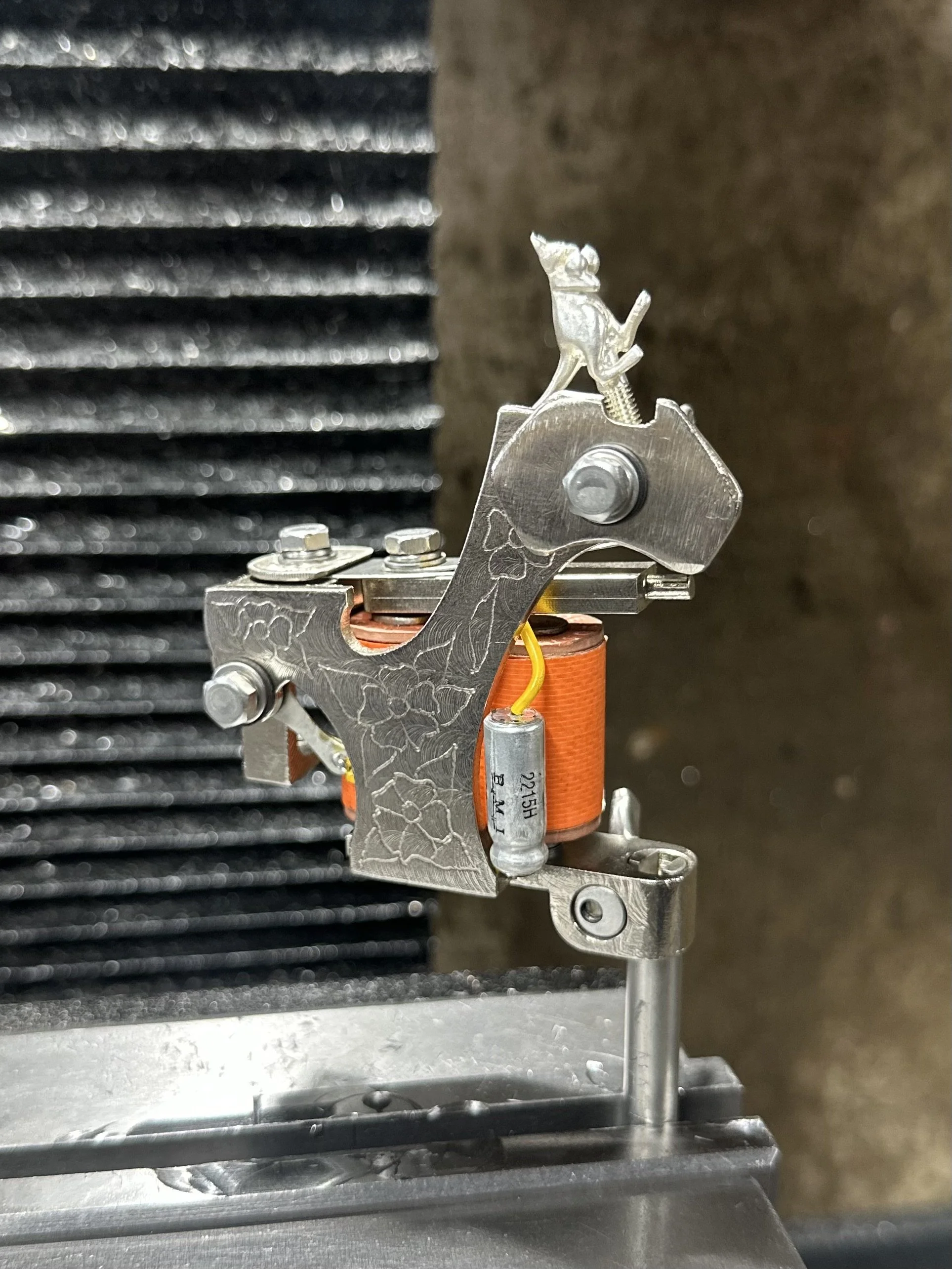 Close-up of a mechanical device with metal parts and a coil, possibly a small motor or engine component, mounted on a metal surface with a black, ridged background.