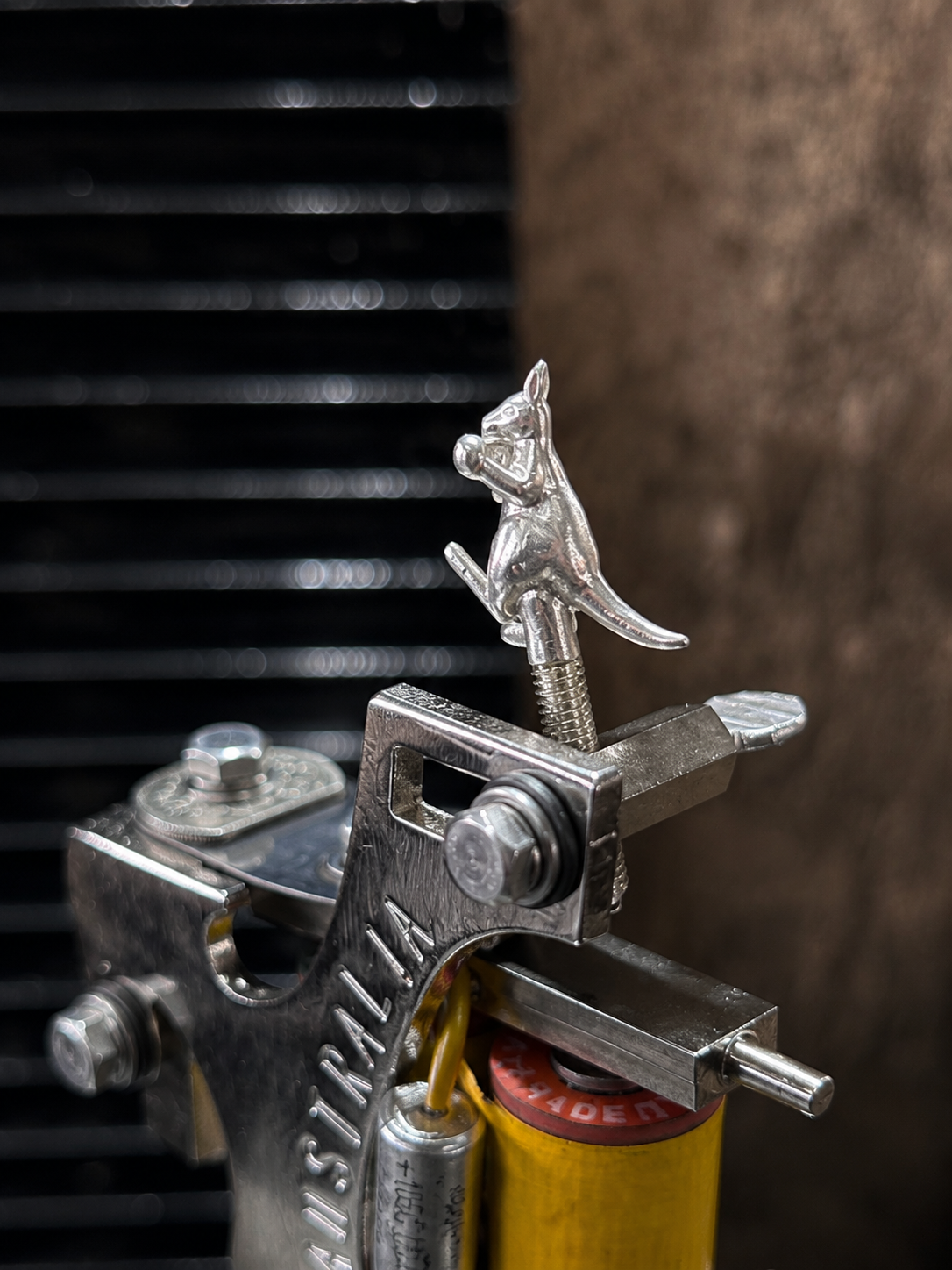 Close-up of a metal latch with a kangaroo figurine on top, attached to a yellow cylindrical object, against a blurry dark background.