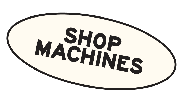 Sign that reads "Shop Machines" in bold black letters on a white background with an oval shape.
