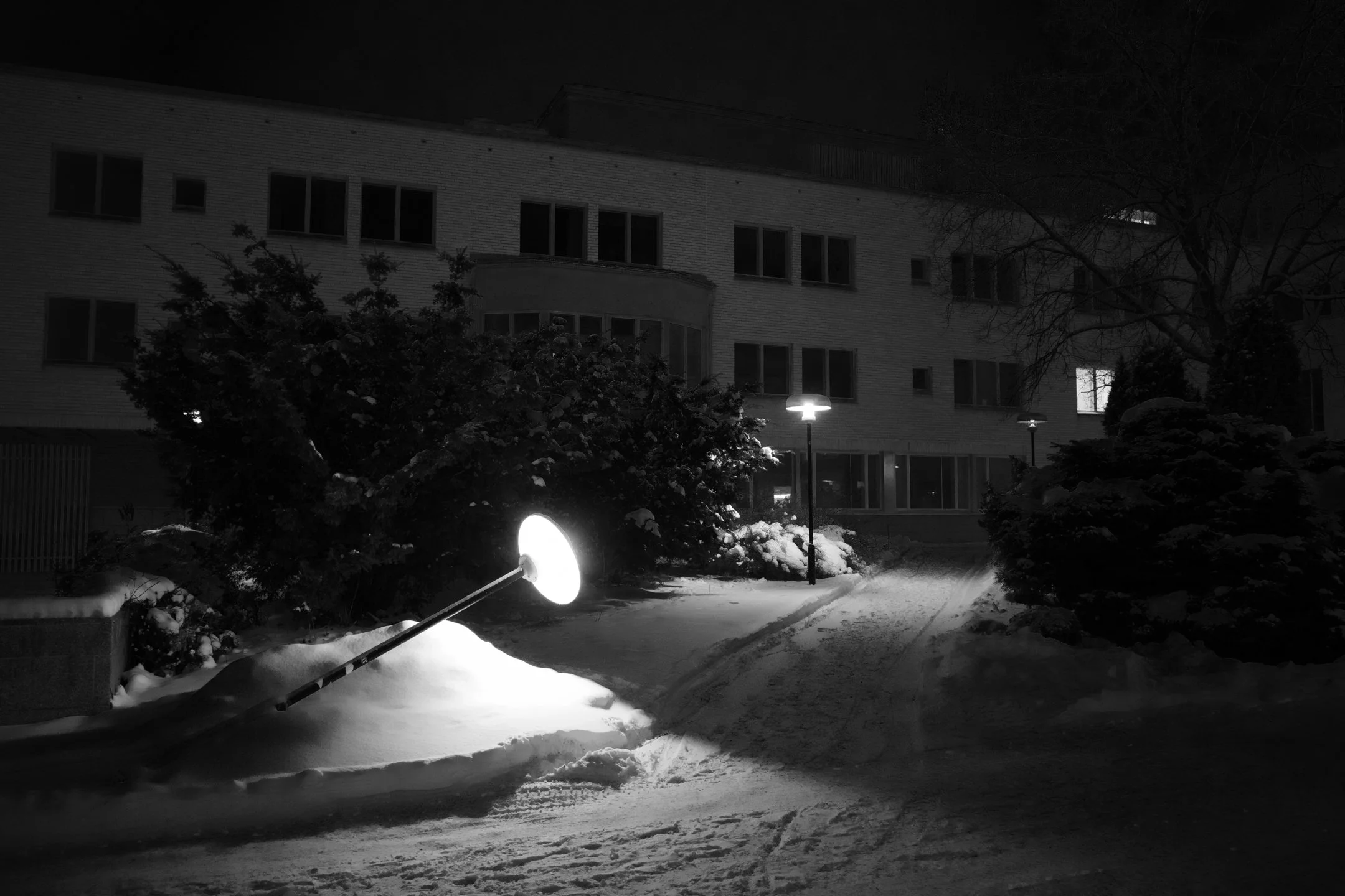 Yökuva lumisesta pihasta, jossa on lämmitettyjä katuvaloja ja rikkinäinen hälytysvalo maassa.