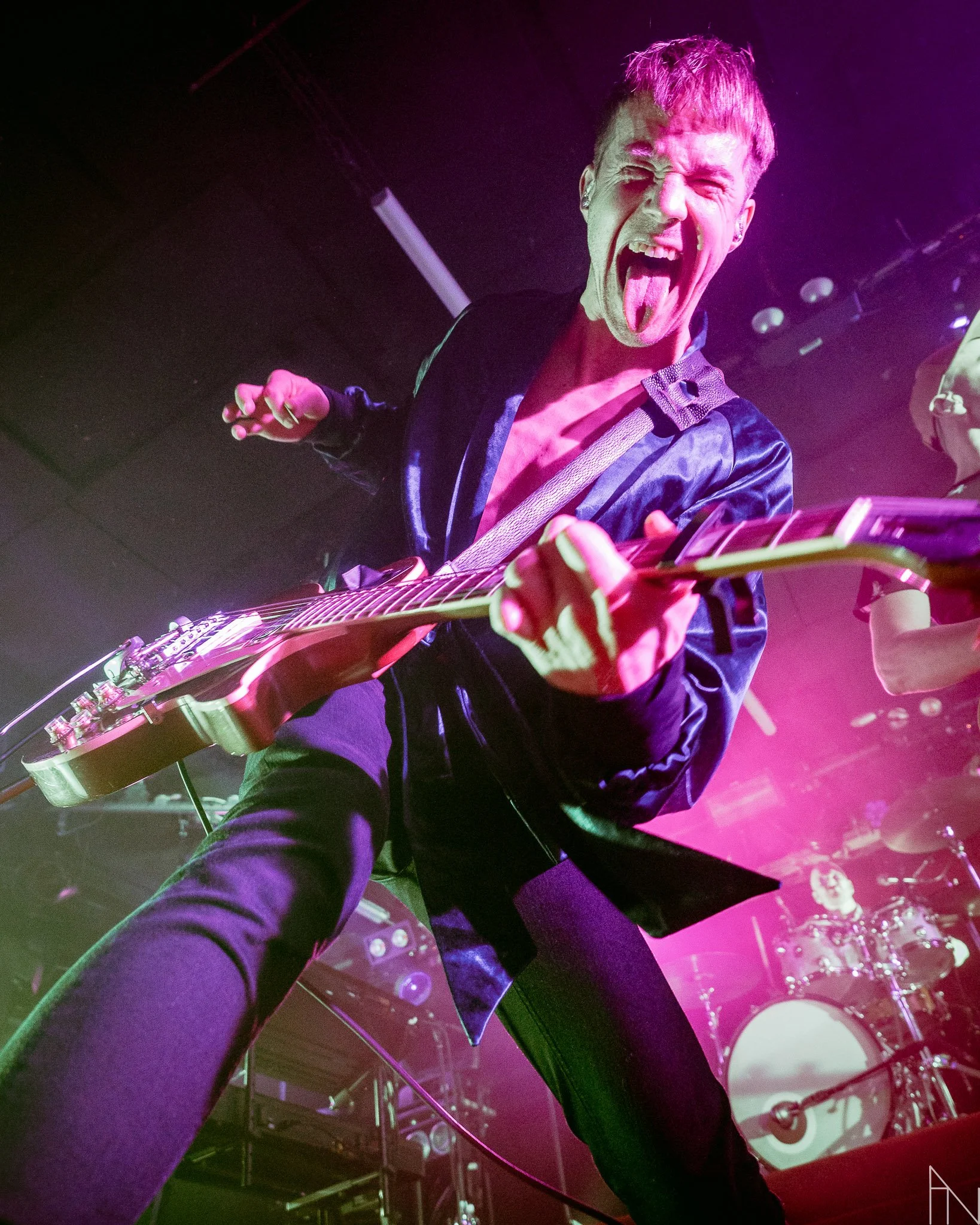 Kuvassa mies soittaa kitaraa lavalla pinkin ja violetin valon keskellä, hän on iloinen ja tekee ilmeen kohti kameraa. Olavi Uusivirta Lutakko 2022.