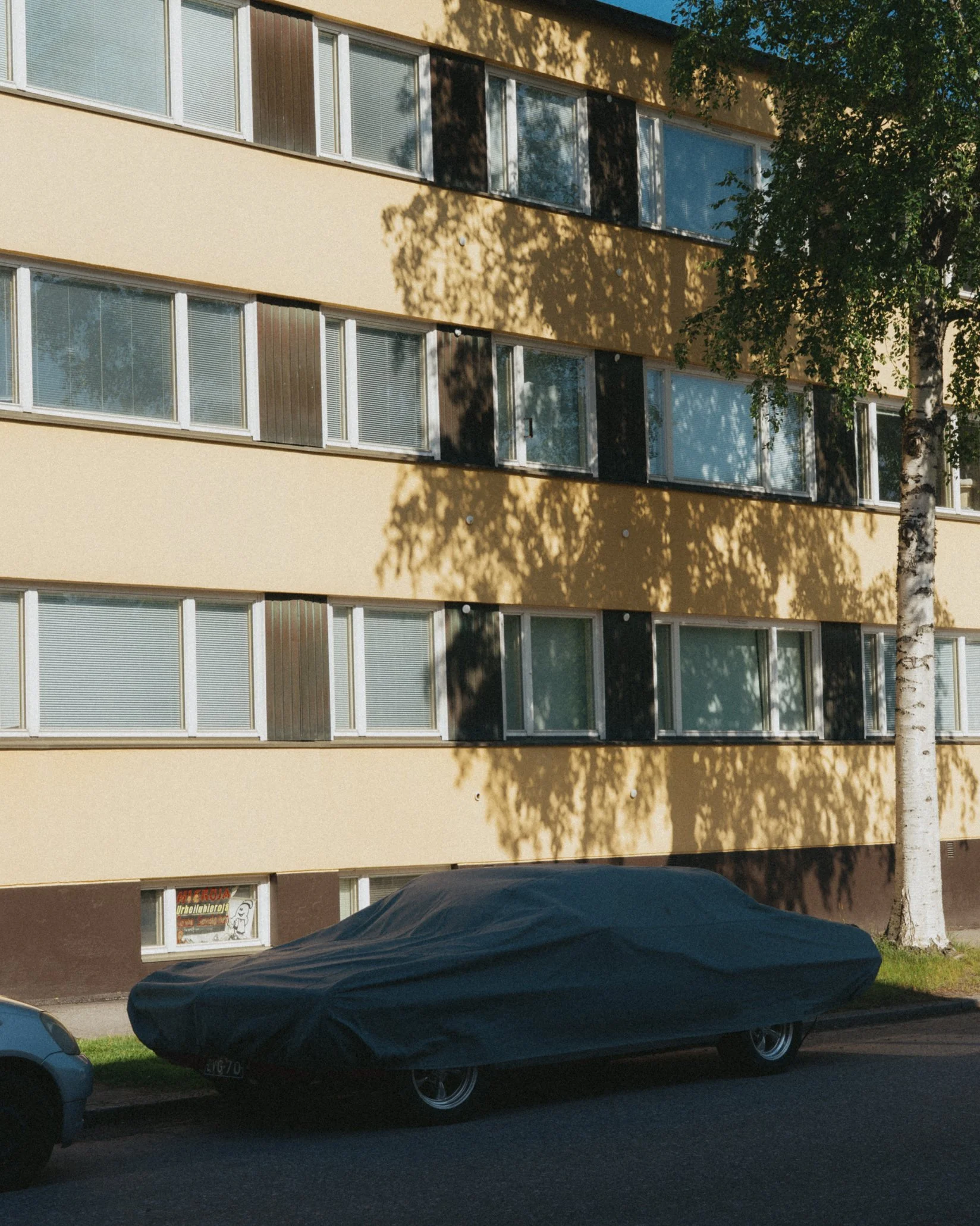 Automobile peitetty suojapeitteellä pysäköity kadun varteen rakennuksen edessä.