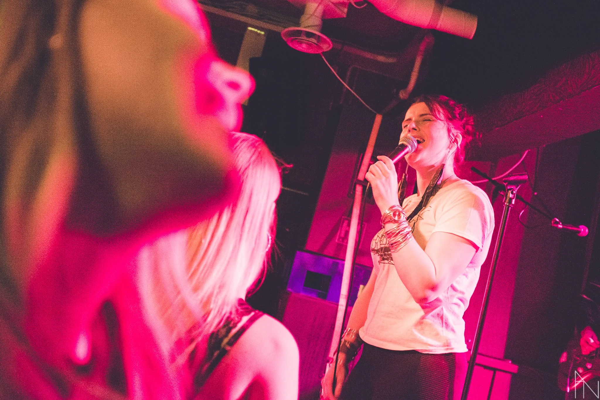 Nainen, Yona, laulamassa mikrofoniin, etualalla laulava fani, hämärä ja punaiset valot, esiintymispaikassa.
