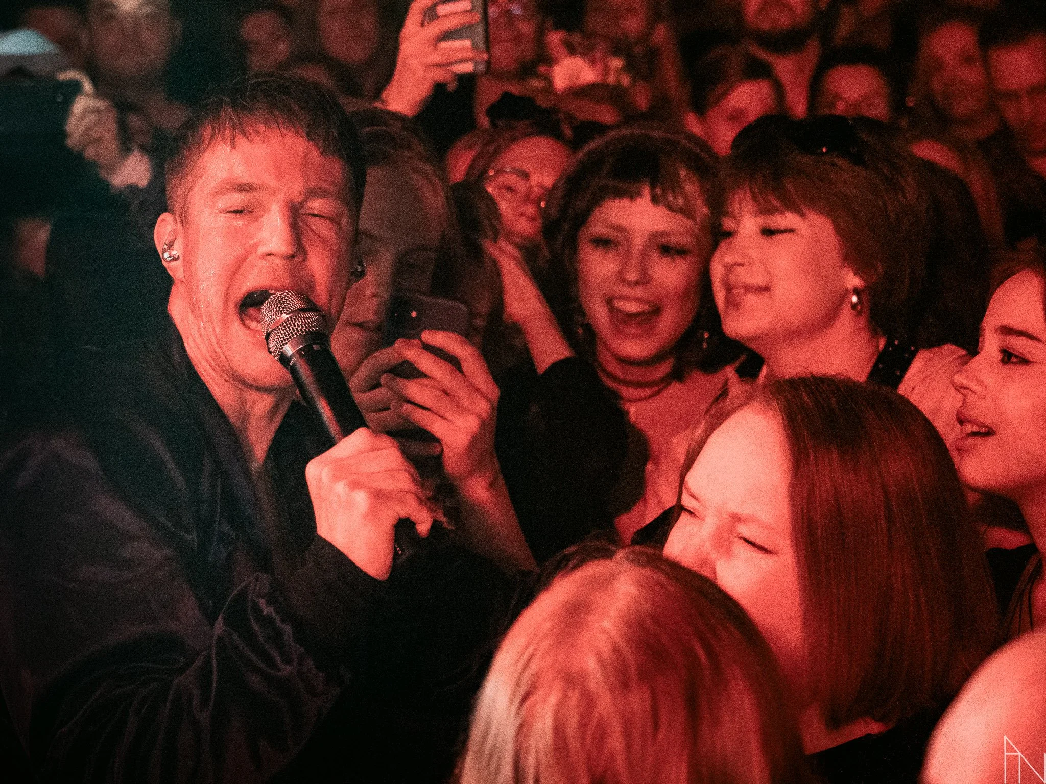 Mies, Olavi Uusivirta, laulamassa mikrofonilla ja ympärillä nauravia ja iloisia ihmisiä konsertissa. Lutakko 2022.