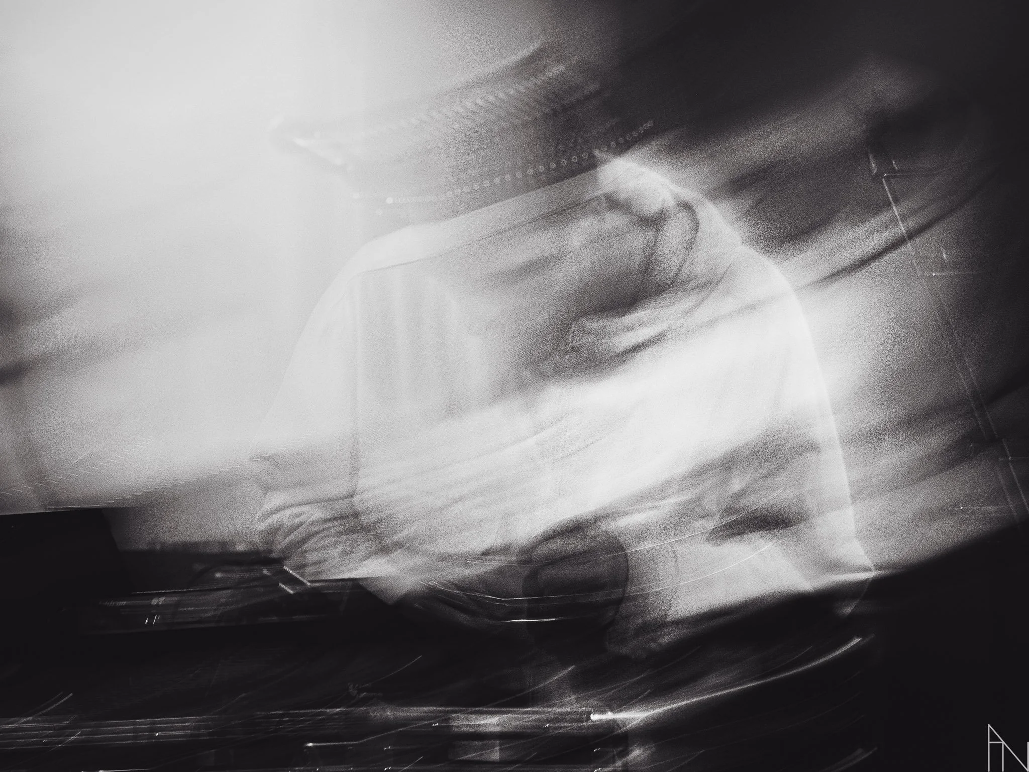 Mustavalkoinen valokuva henkilöstä, jonka kasvot ja keho ovat epätarkkoja ja liikkuvia, mahdollisesti kuvattu pitkällä valotusajalla.