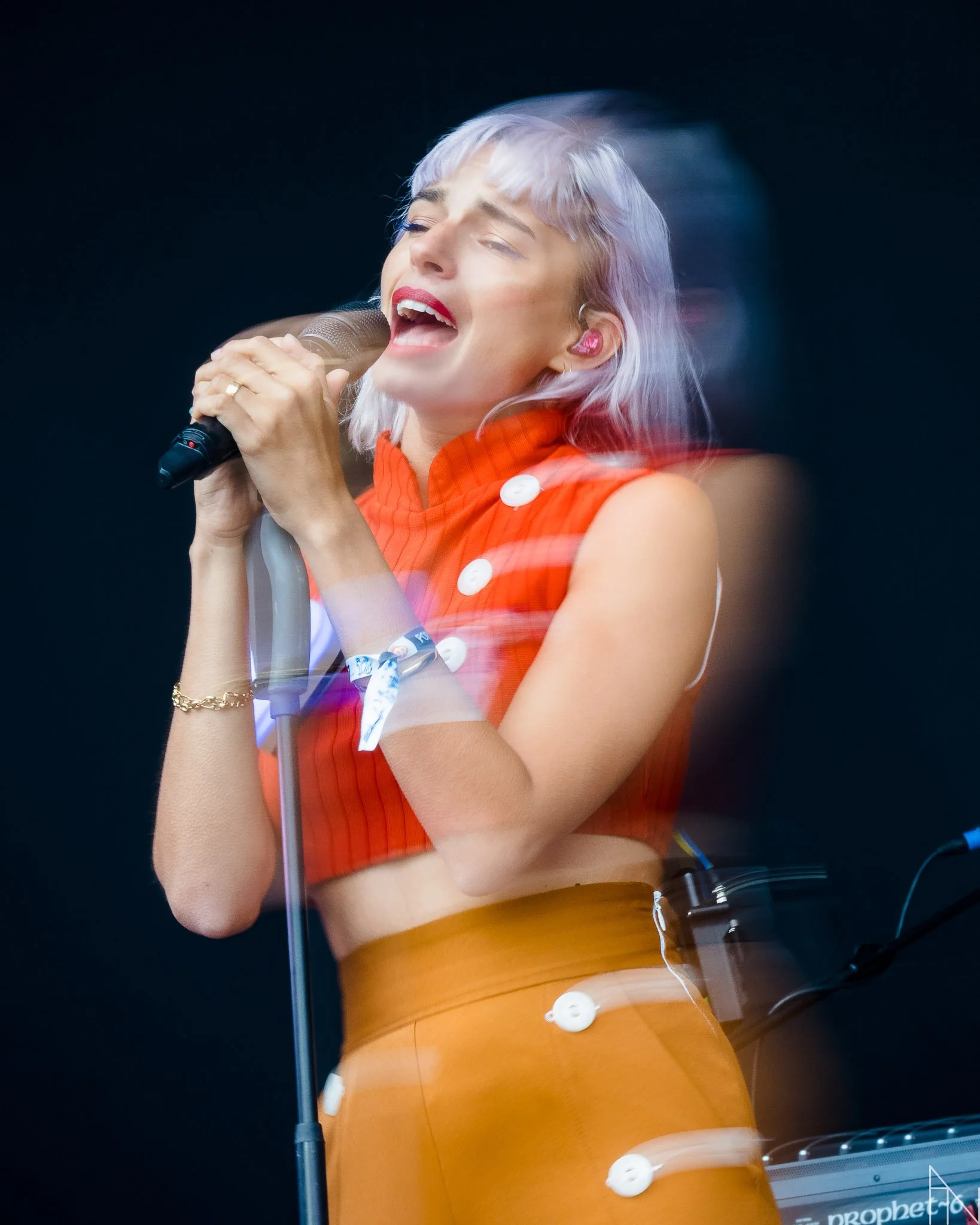 Nainen laulamassa mikrofoni käsissään, pimeällä taustalla, esiintymisasussa.