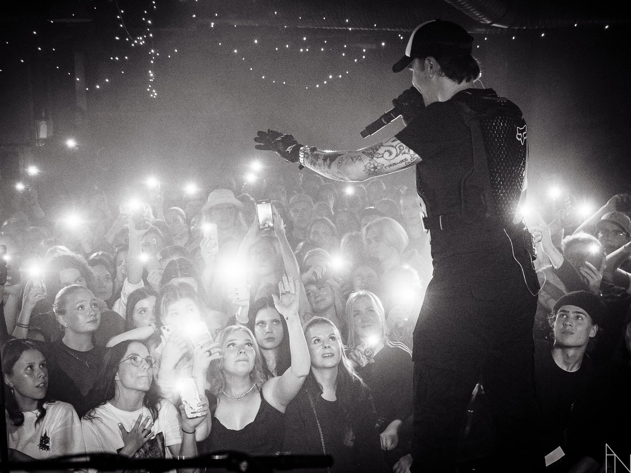 Lavalla oleva laulaja tai esiintyjä ja suuri yleisön joukko, jonka ihmiset ovat ottamassa kuvia tai videoita älypuhelimillaan. Näkyy tummia ja kirkkaita valoja. Lauri Haav Lutakko.