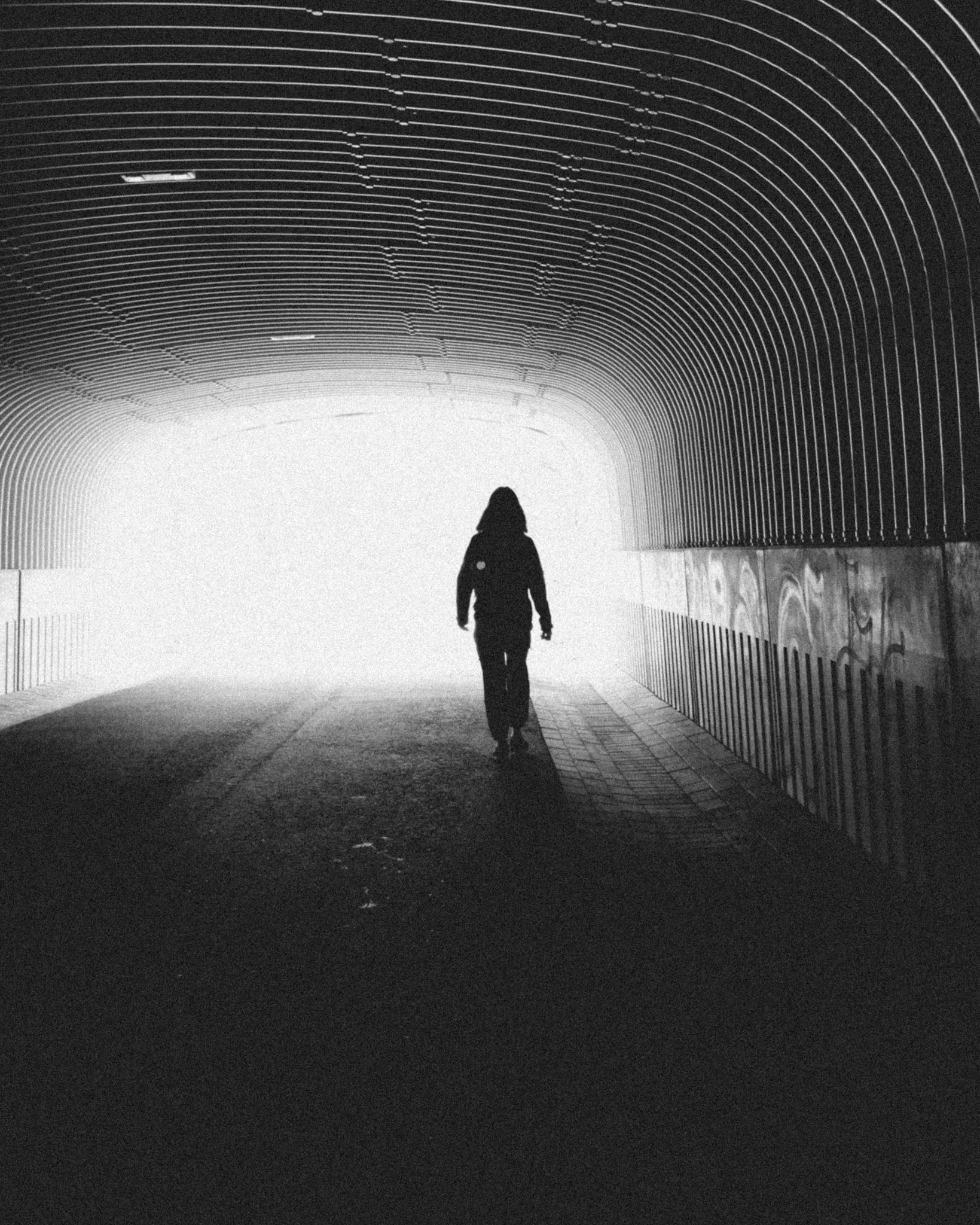 Harmaavalkoinen kuva henkilöstä kävelemässä tunnelissa kohti valoa.