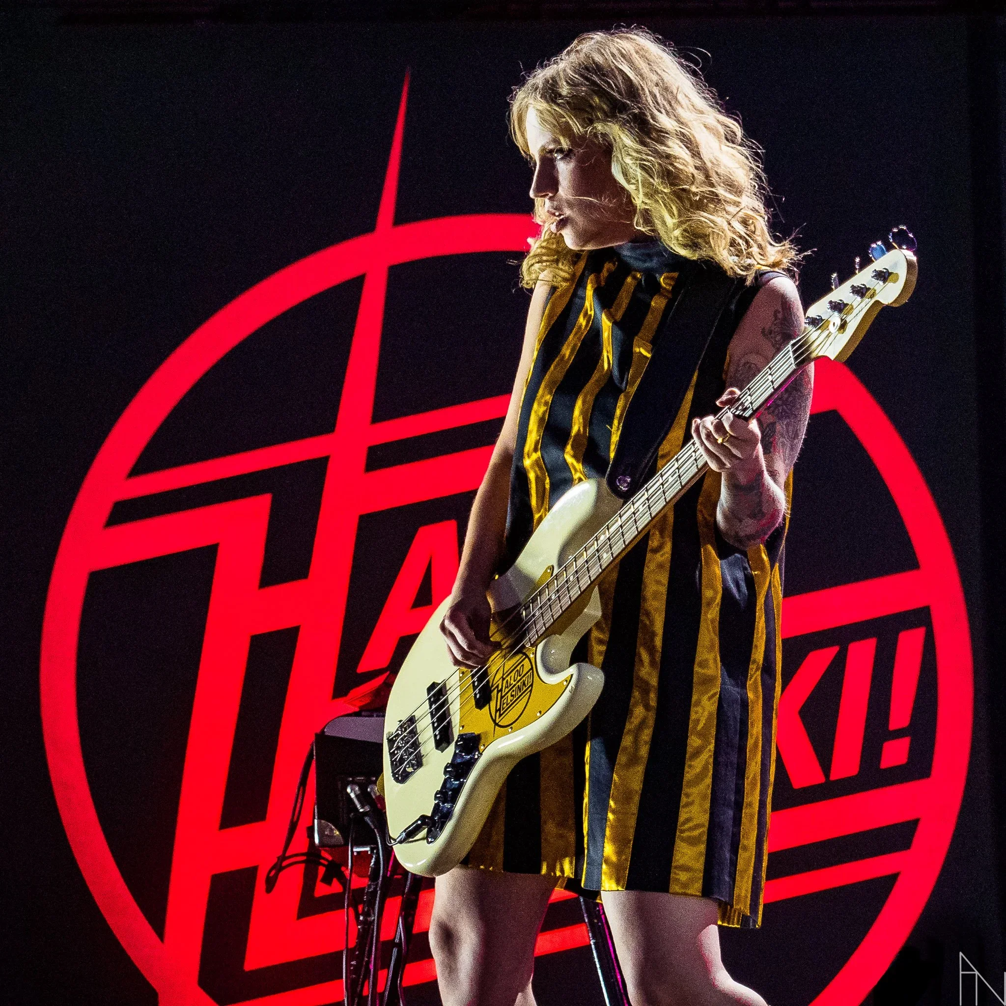 Nainen soittaa kitaralla lavalla, taustalla punainen Haloo Helsinki -logo. Elli Haloo.