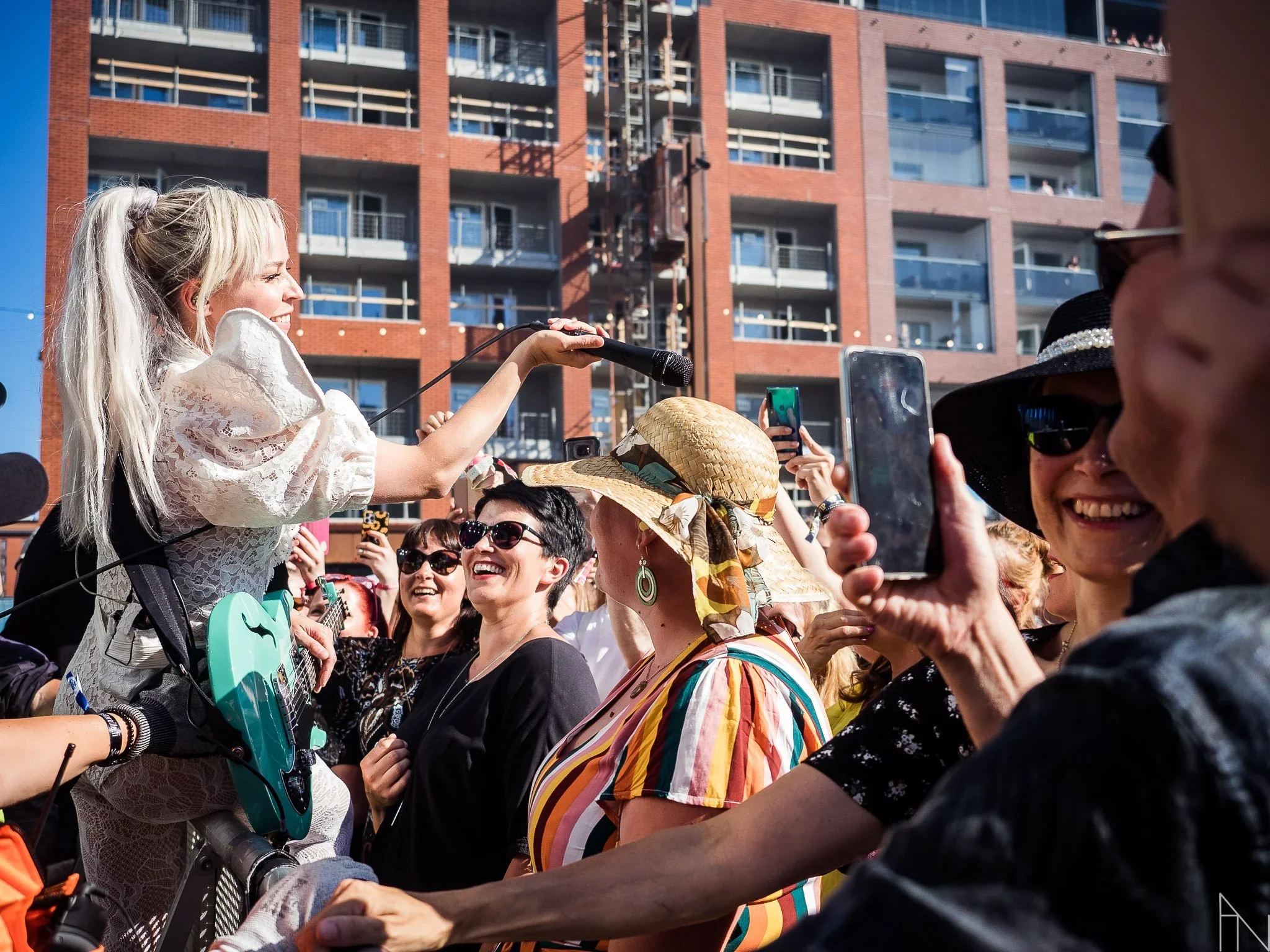 Paula Vesala esiintyy elävän yleisön edessä ulkotapahtumassa, taustalla kerrostalo ja rakentaminen.