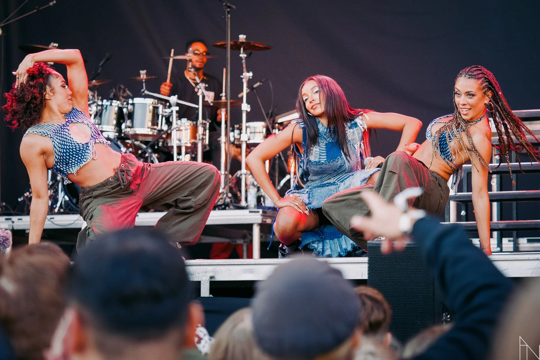 Kolme naisvartaloa esiintymässä tanssiesityksessä lavalla, taustalla rumpali.