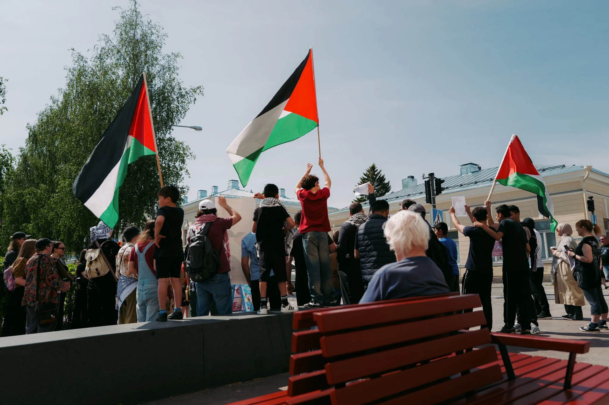 Ihmiset juhlivat ulkona, osassa heiluu palestiinalaisia lippuja, taustalla rakennuksia ja suuri puu.