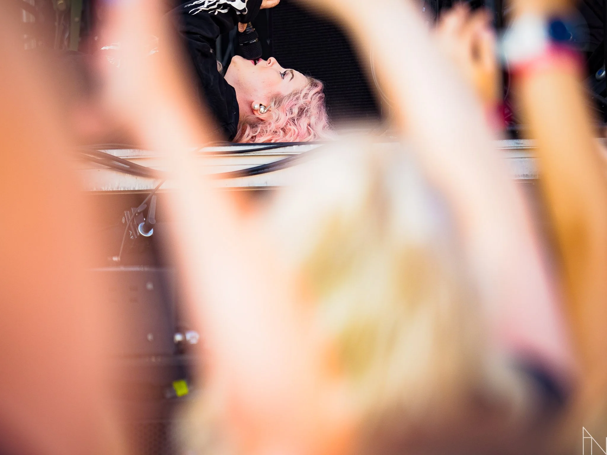 Kuva naisesta, joka makaa maassa ja puhuu mikrofoniin, kuvassa on myös muita ihmisiä ja valonheitimiä.