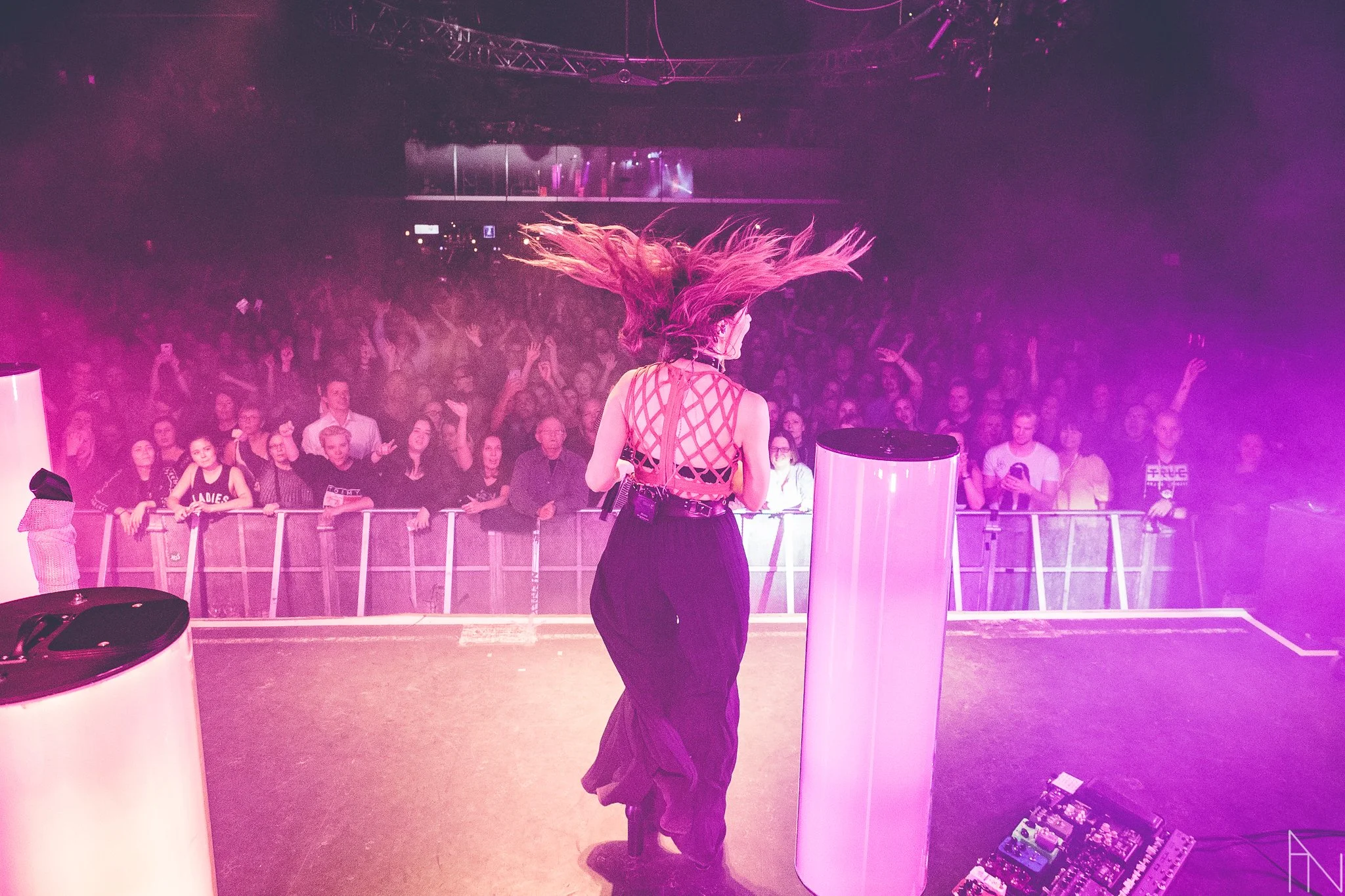 Nainen esiintymässä lavalla, hänen hiuksensa heilahtavat, edessä musiikkilaitteet ja suuret valopilarit, taustalla suuri yleisö juhlimassa. Jenni Vartiainen kuvattuna lavalta.