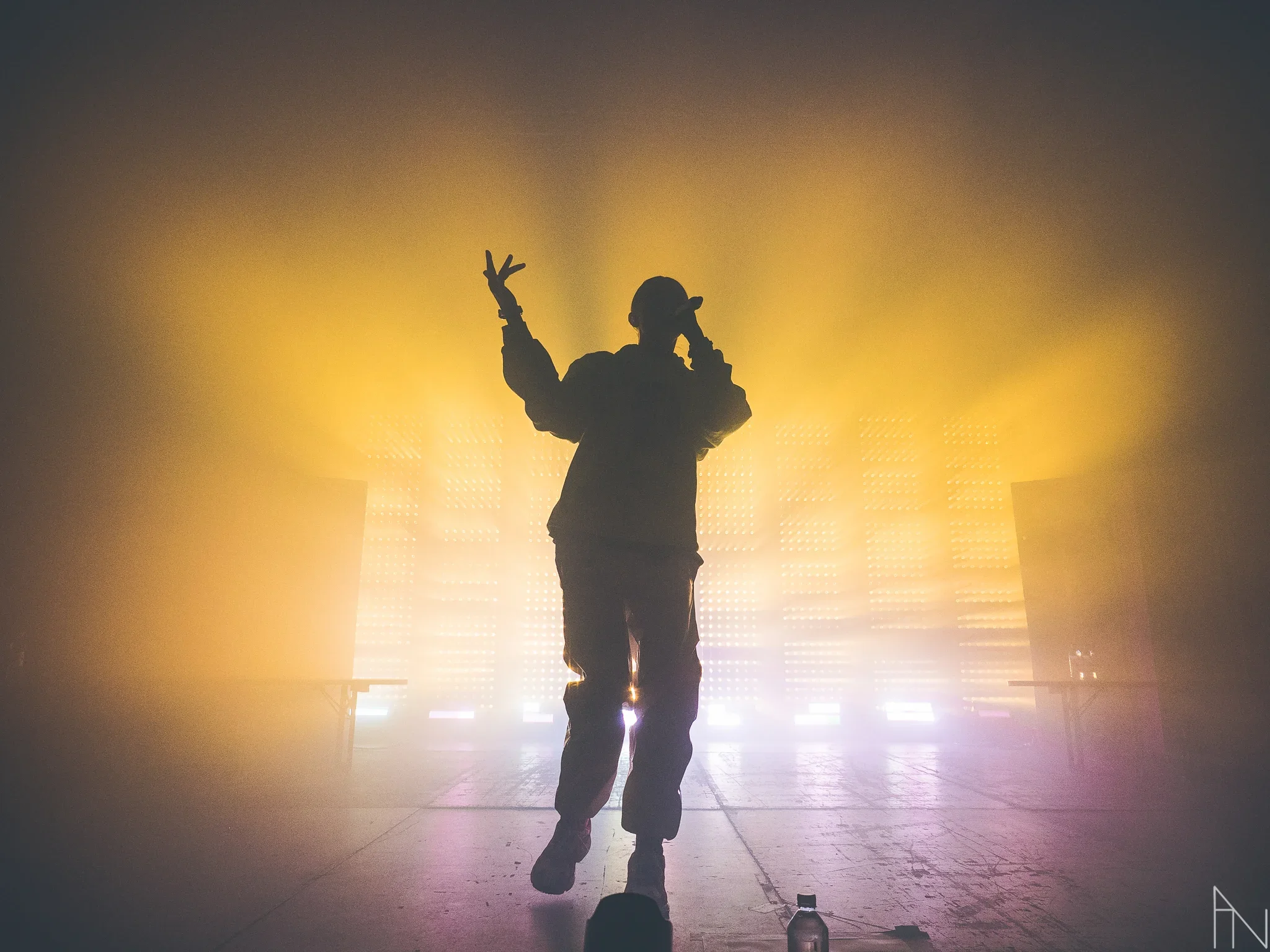 Silhuetti tanssijasta tai artistista valaistuksessa, taustalla valoja ja savua, lavalla