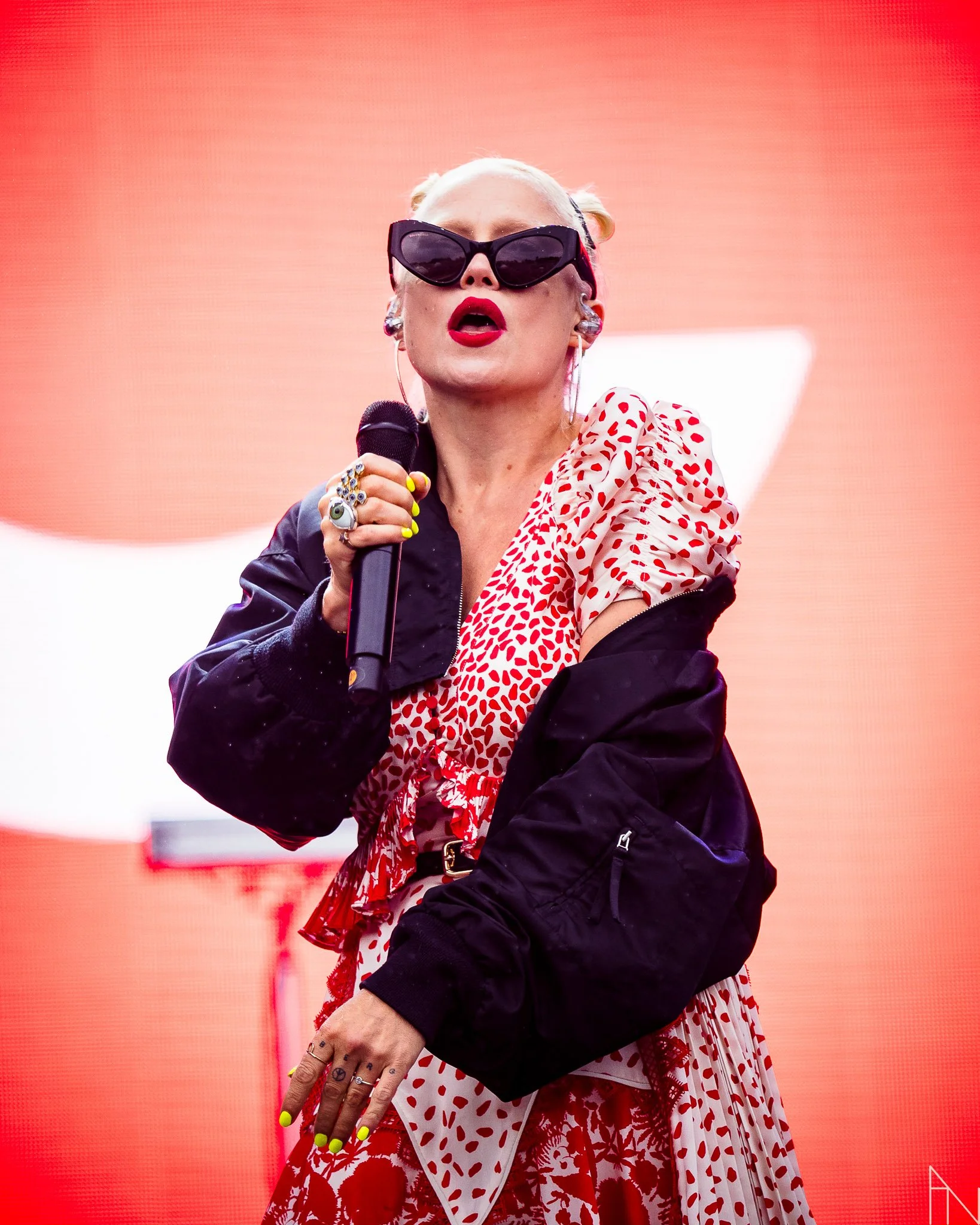 Nainen esiintymispuvussa, jossa punainen ja valkoinen kuvio, ja musta takki, pitäen mikrofonia.
