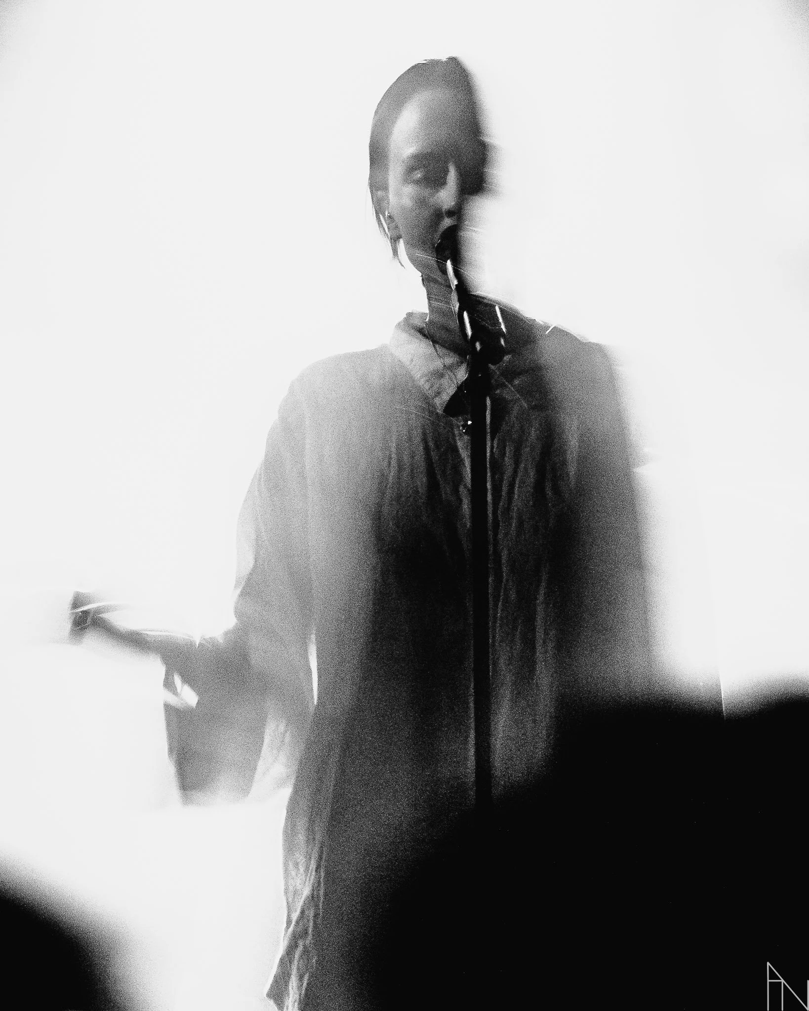 Musta ja valkoinen kuva naisesta, Pehmoaino, joka pitää mikrofonia, taustalla valoisa tila ja hieman epätarkka, häilyvä ympäristö. Lutakko 2022.